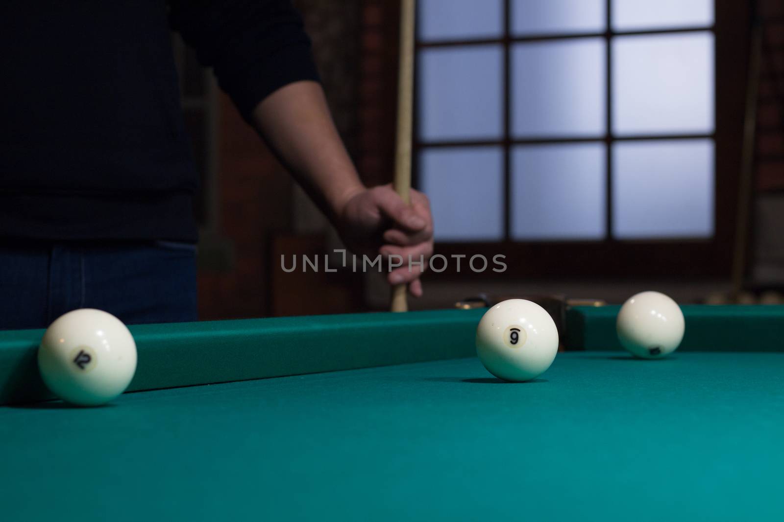 Close-up of Russian billiards game in process: three white balls on green game table cloth and player with cue on background