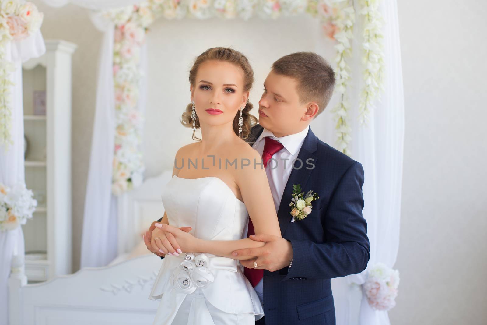 Stylish newly-married couple standing embracing in bedroom