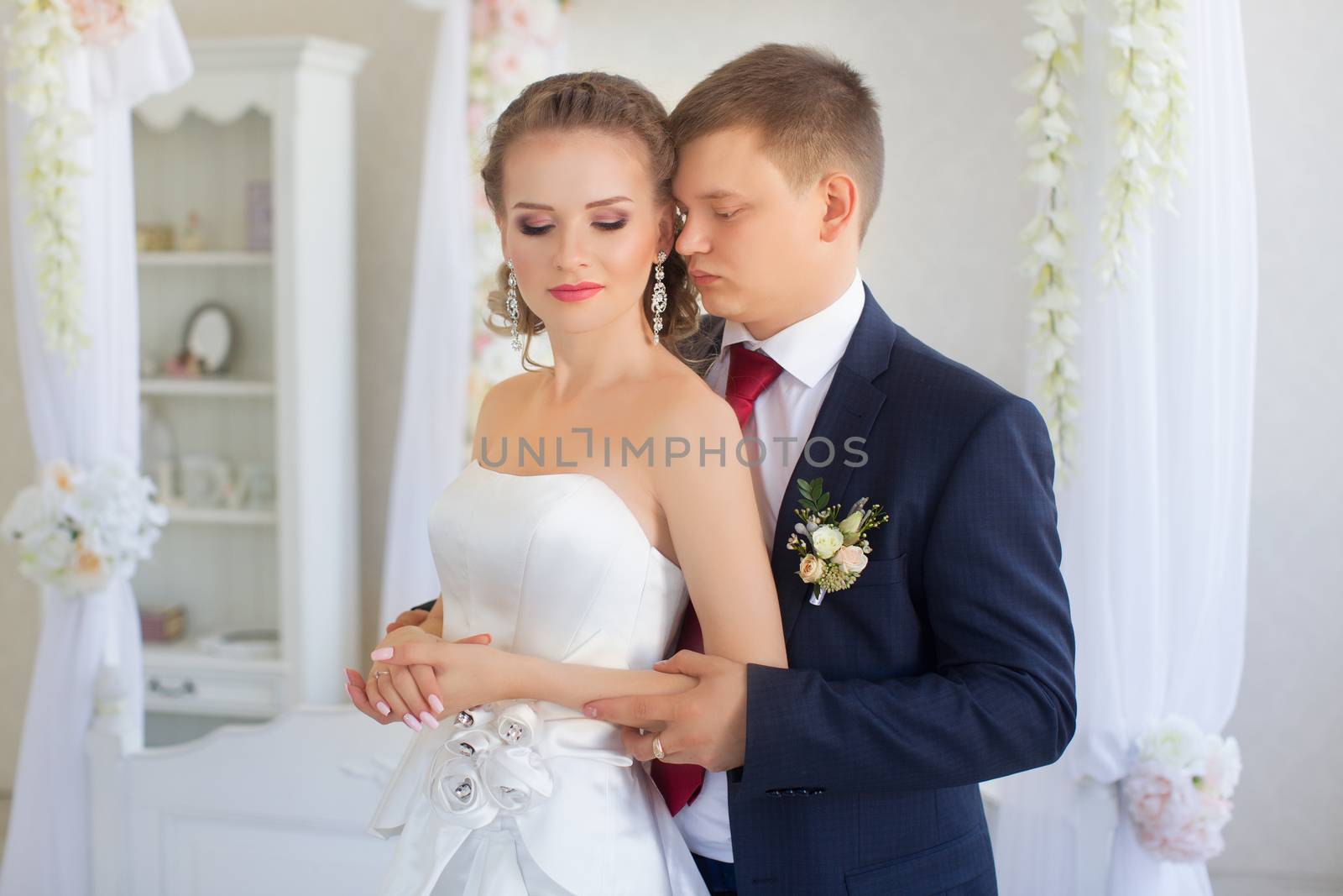 Stylish newly-married couple standing embracing in bedroom