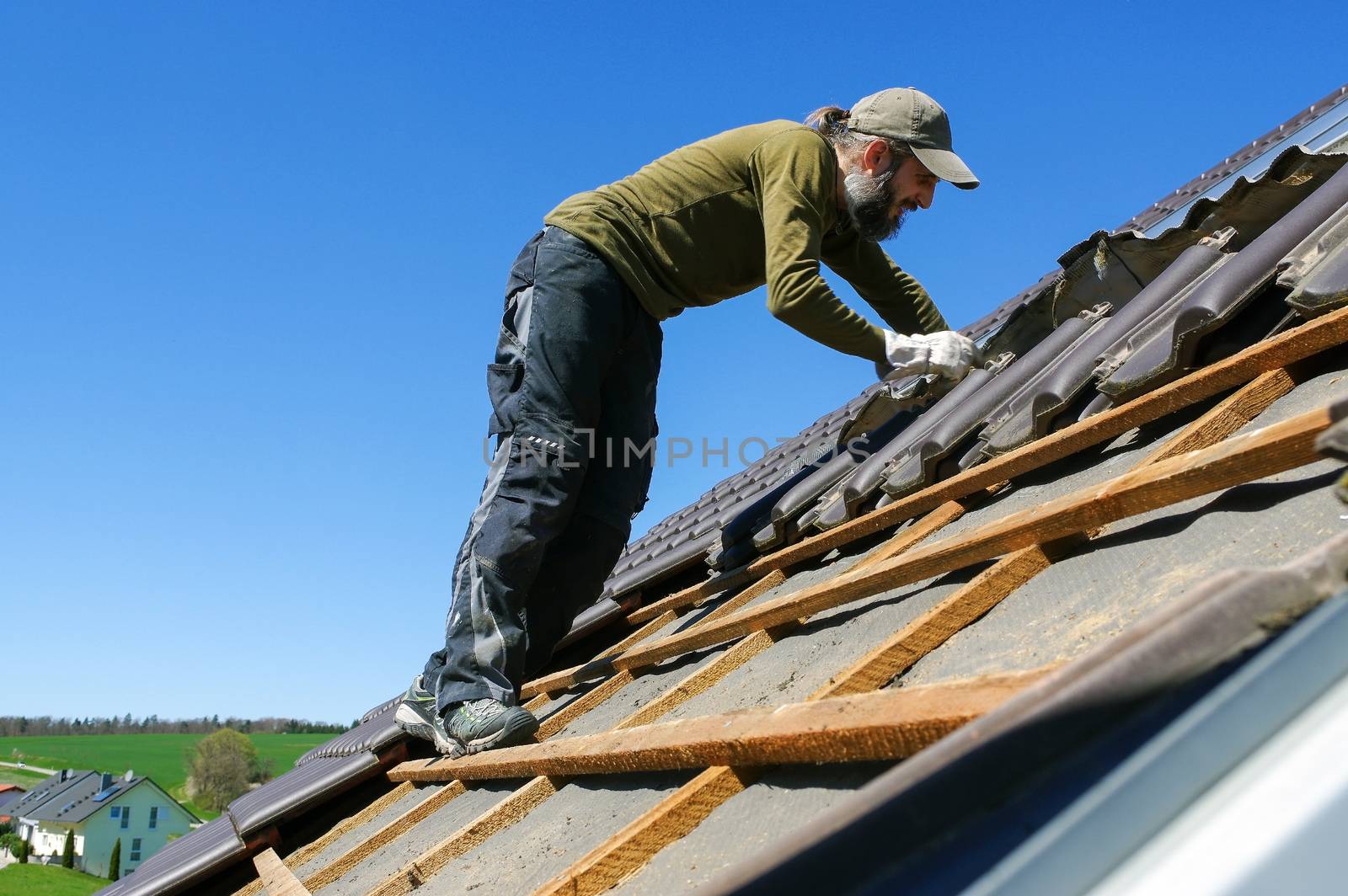 roofer laying tile on the roof by evolutionnow
