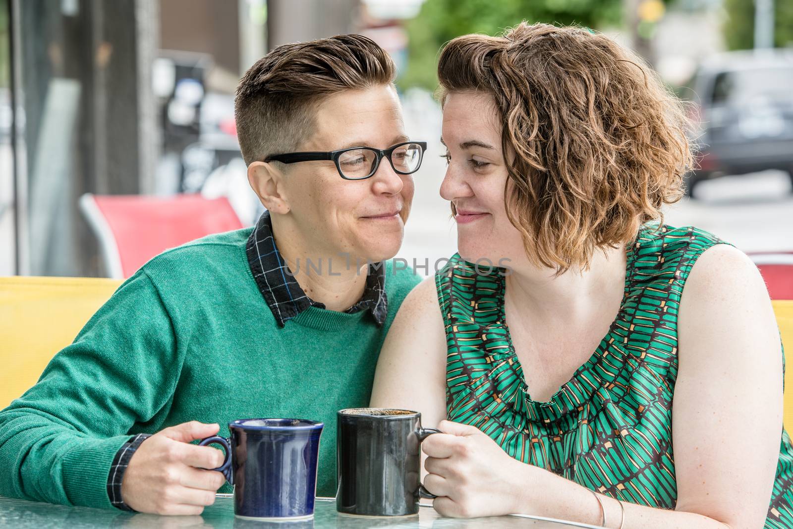 Joyful lesbian couple looking at each other while seated outside