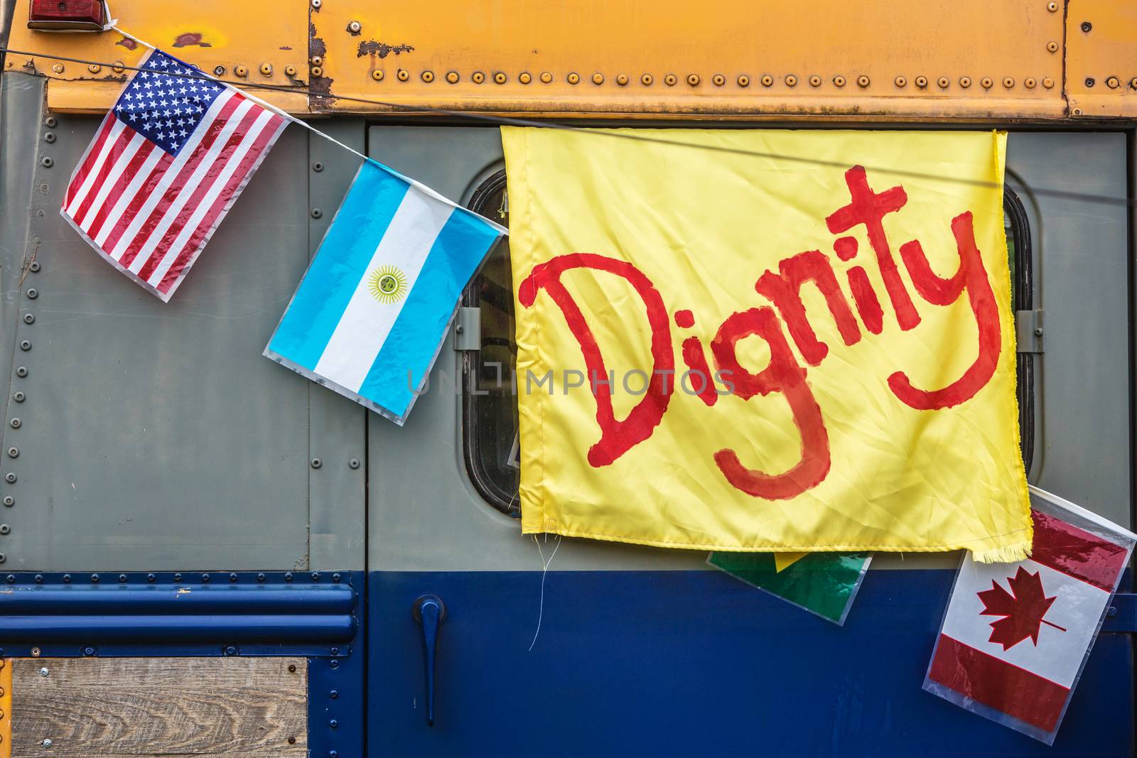 Yellow dignity banner with various flags hanging from side of old school bus