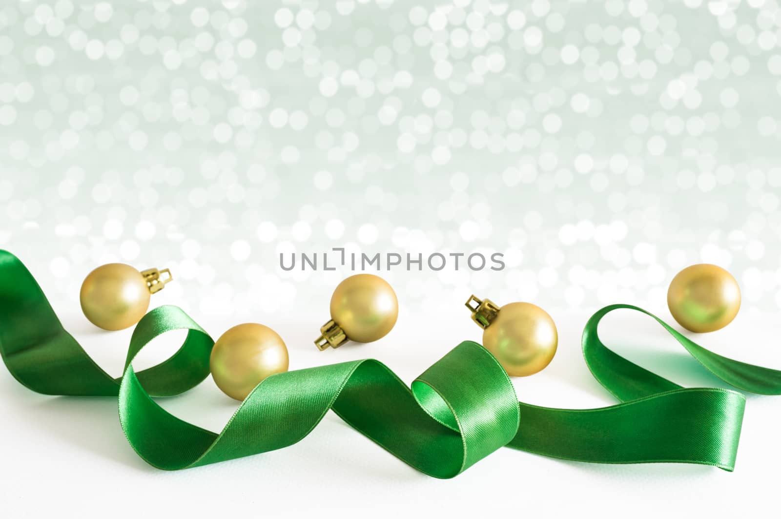 Golden christmas balls with green ribbon with lights snow winter background. Space for copy.