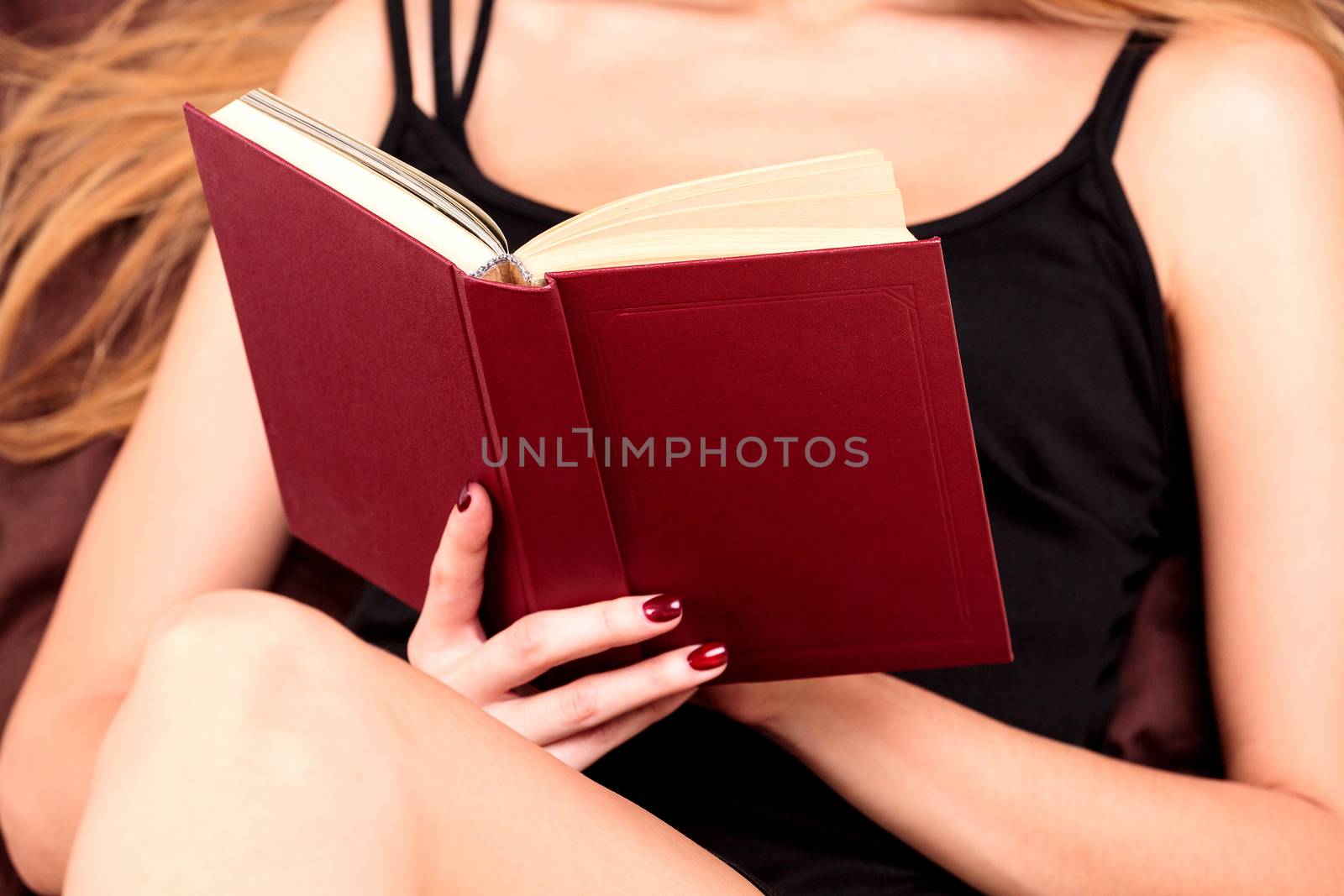 close up of young woman reading book in bed by Nobilior