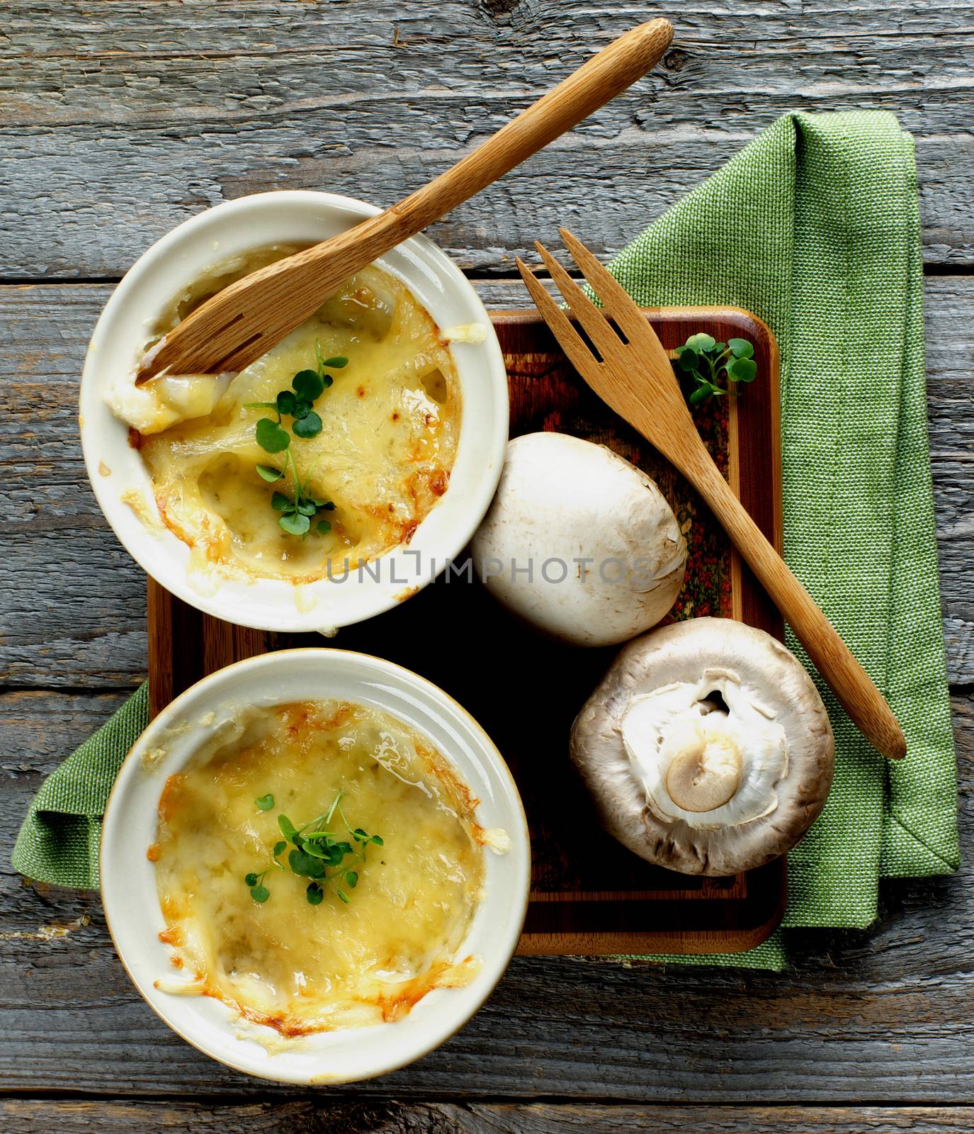 Arrangement of Delicious Champignon Mushroom Julienne in Ramekins with Wooden Forks and Napkin on Rustic Wooden background