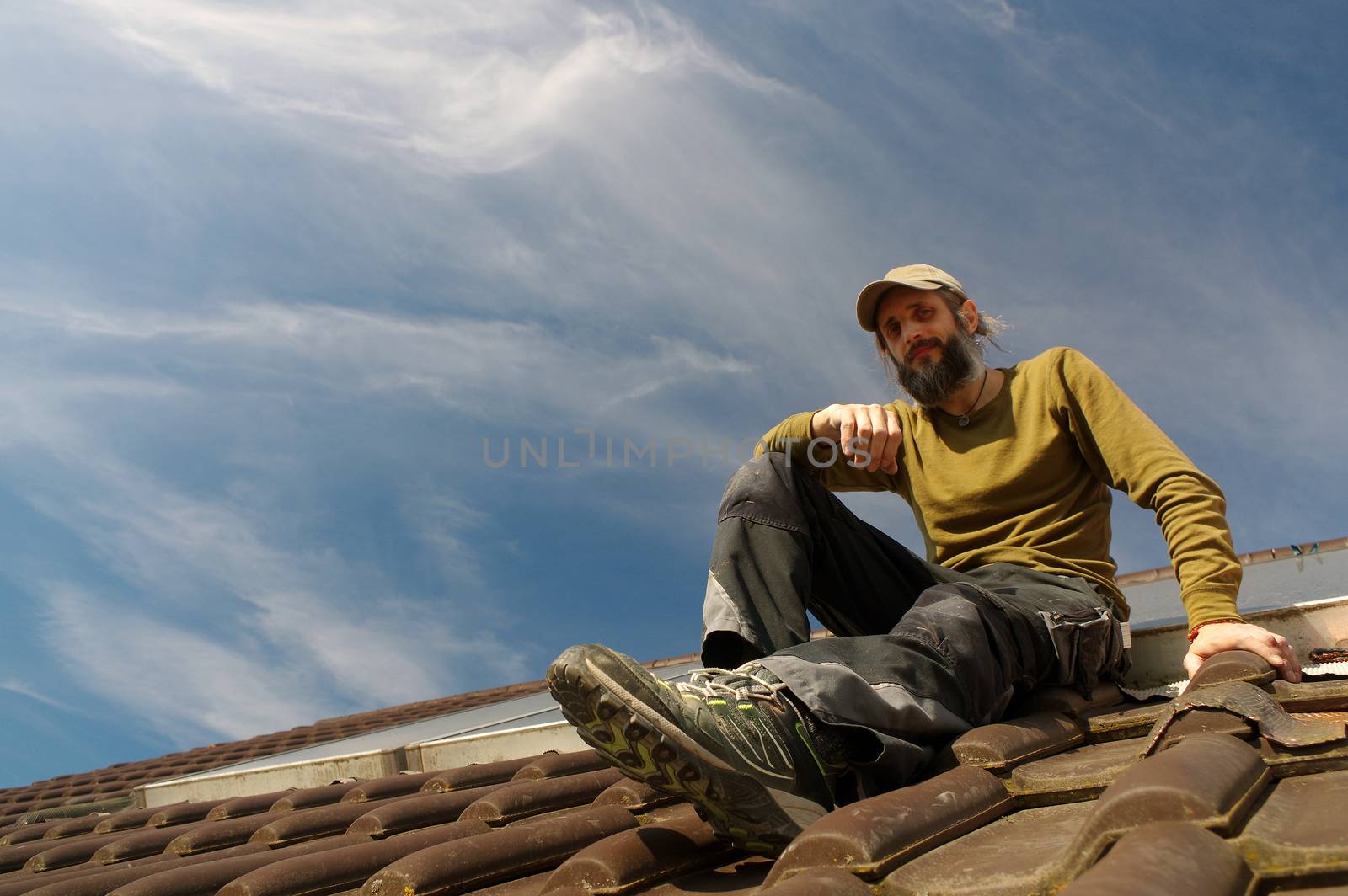 bearded roofer resting on top of a roof sunny day by evolutionnow