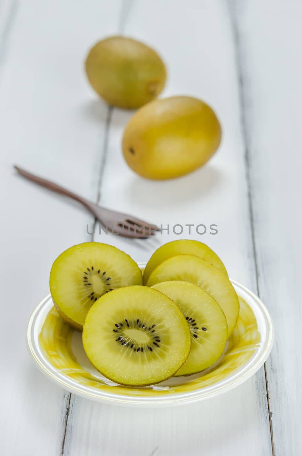 golden kiwi fruit and sliced on dish over white wooden background