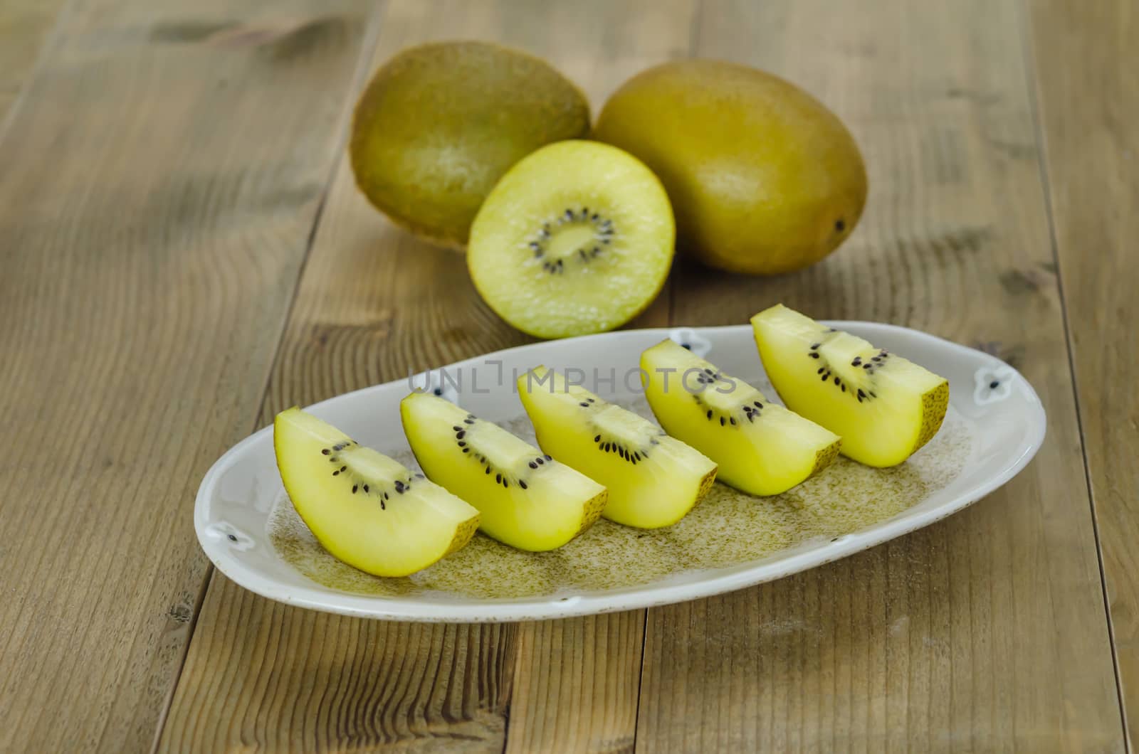 golden kiwi fruit and sliced on dish over wooden background