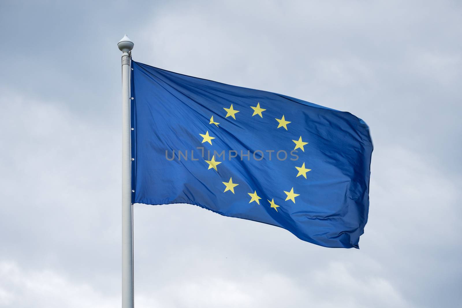 The flag of the European Union fluttering on wind against the background of gray clouds.