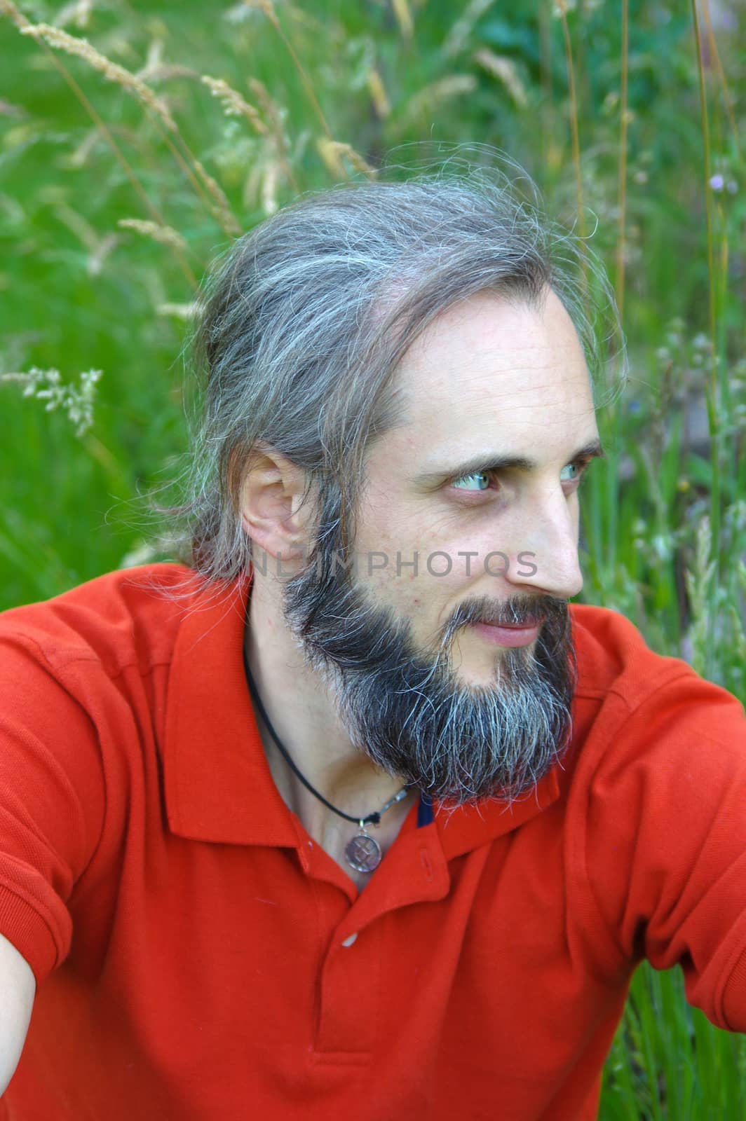 Young bearded man sitting out side on sunny day with green background. This is a portrait by evolutionnow