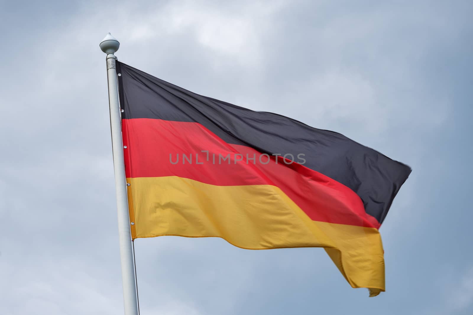 The flag of Germany flutters on wind against the background of gray clouds.