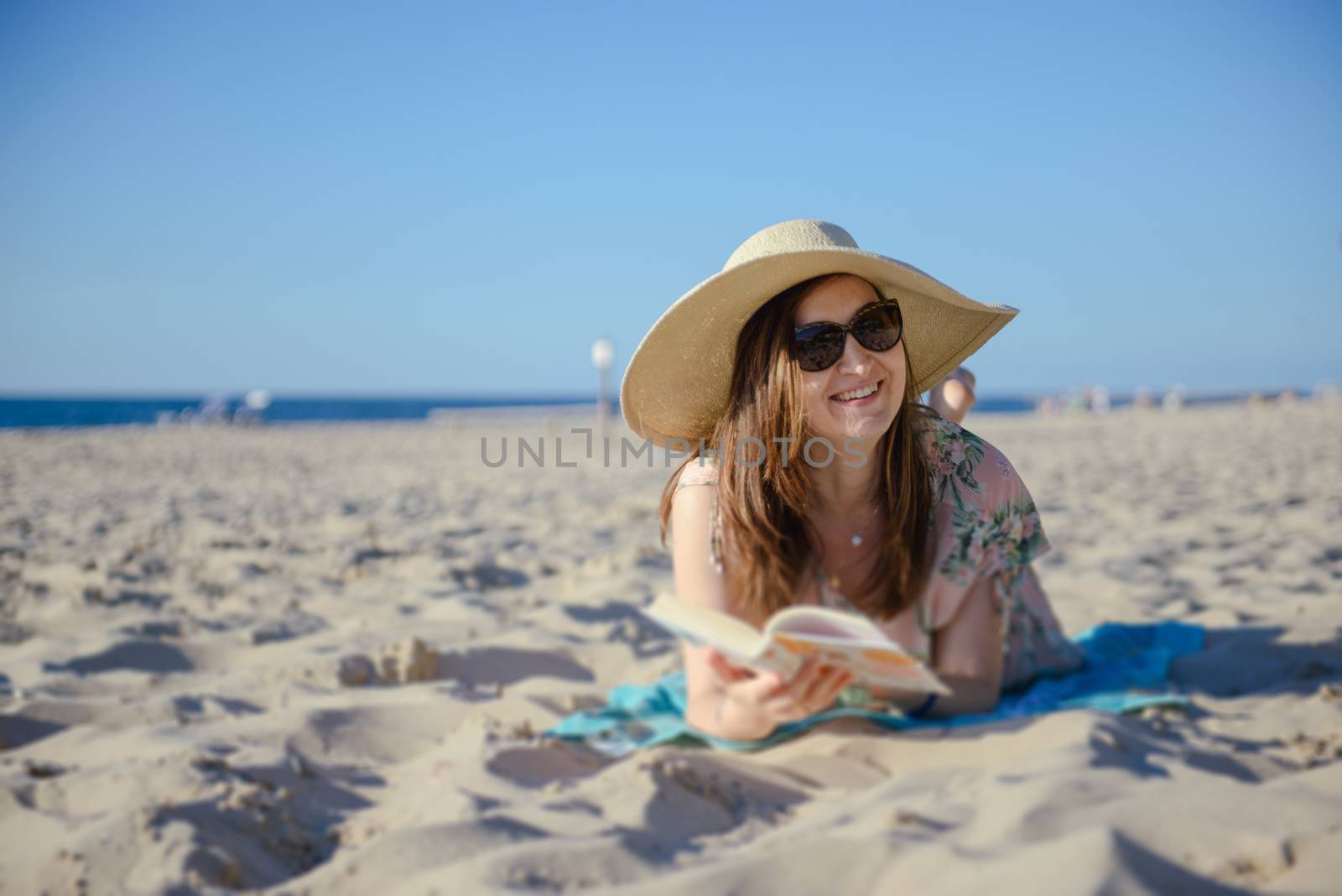 Portrait of a young brunette relaxing on the beach, reading a book. Summer time