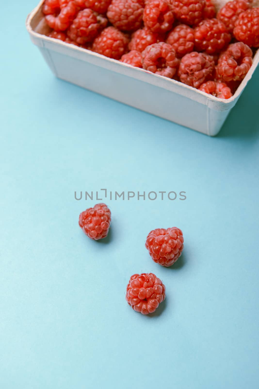 box of fresh raspberries on a blue background