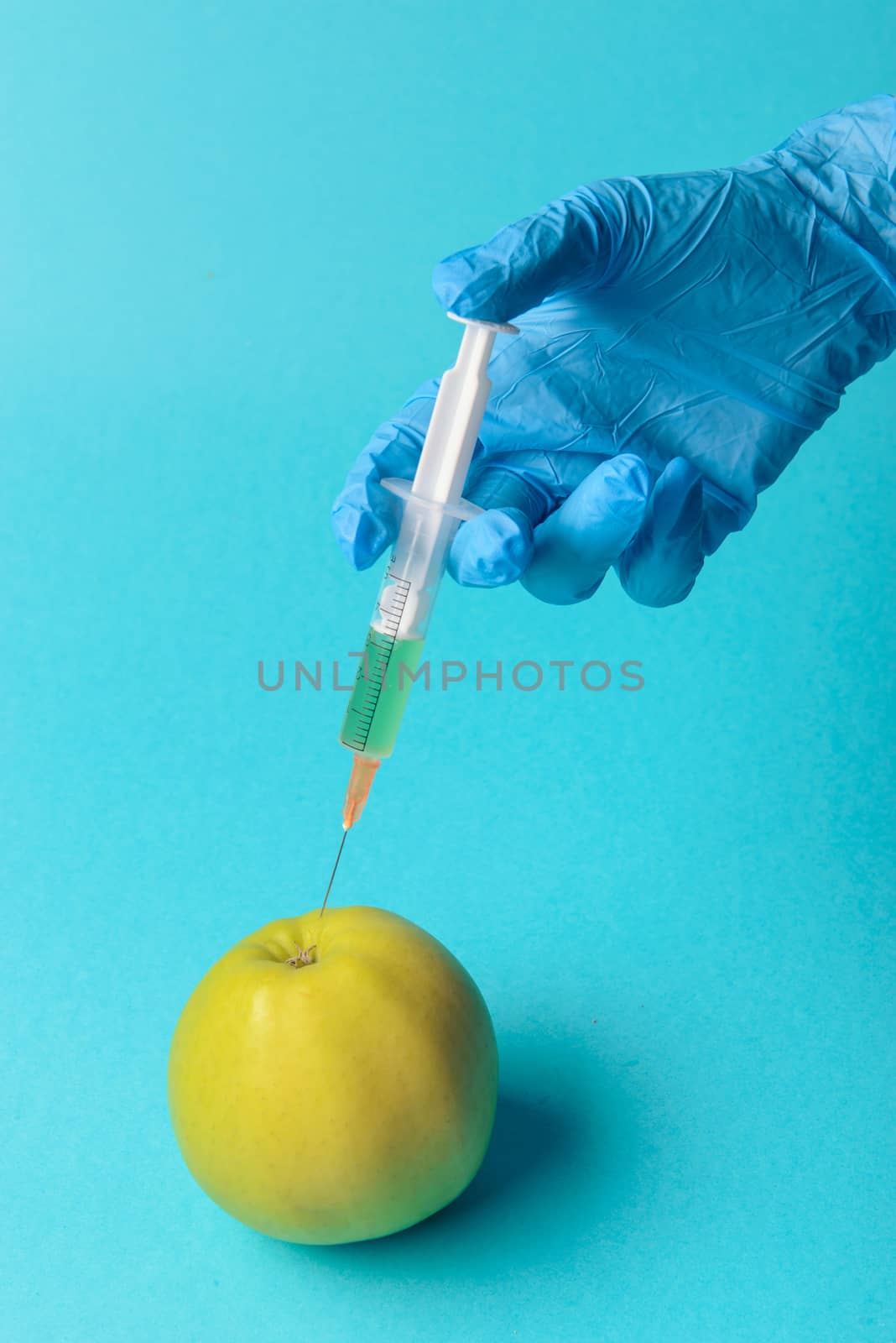 Chemical additives in food or genetically modified fruit concept. Green apple with syringes of chemicals. Isolated on blue background.