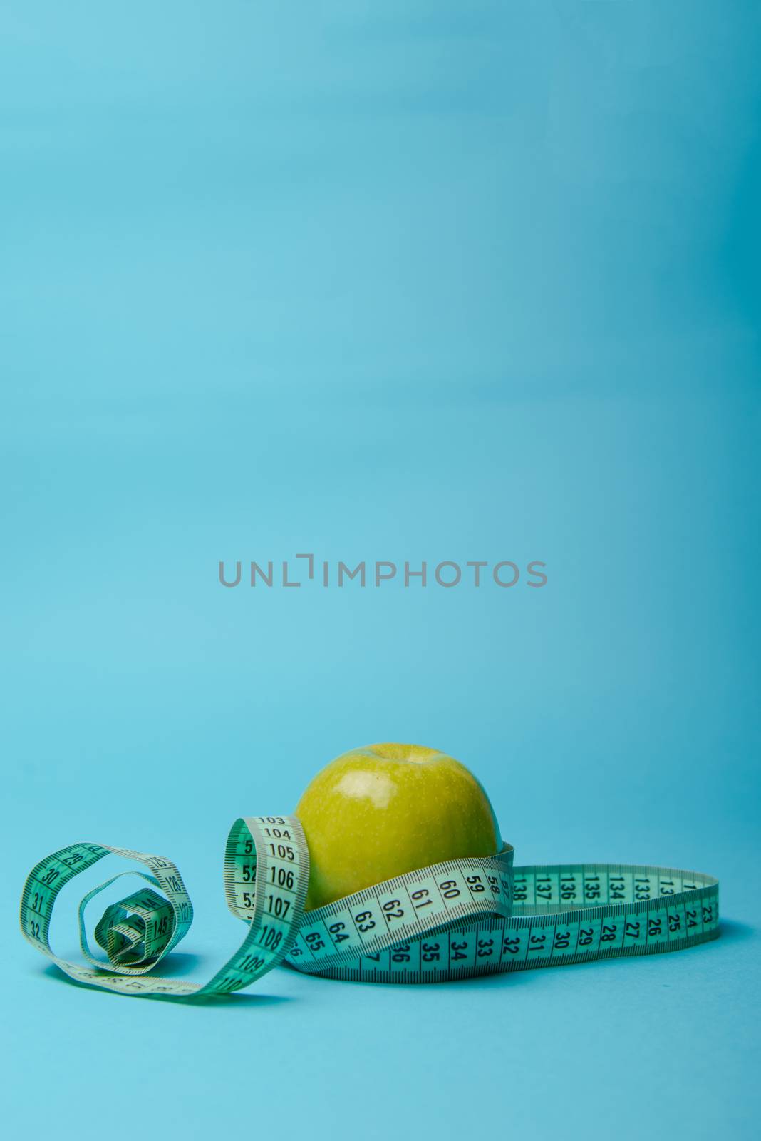 Green apple with measuring tape on blue background