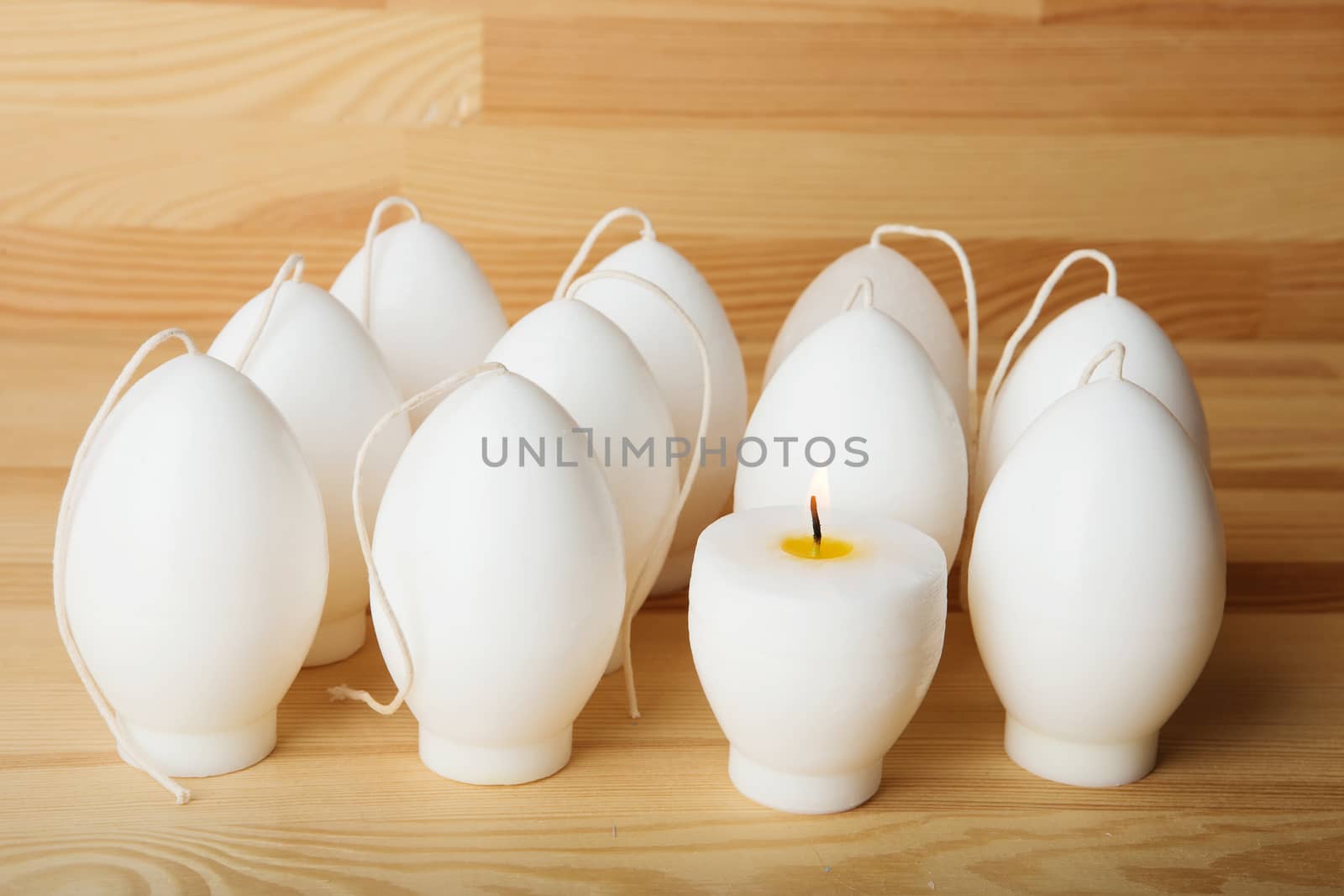 Decorative Handmade candles in the shape of eggs ready for painting and decorating for the holiday. White candles on wood background with copy-space. Candle lit. Happy Easter