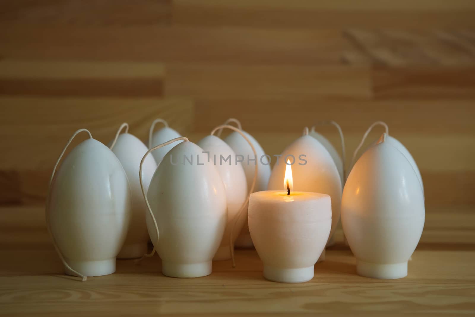 Decorative Handmade candles in the shape of eggs ready for painting and decorating for the holiday. White candles on wood background with copy-space. Candle lit. Happy Easter
