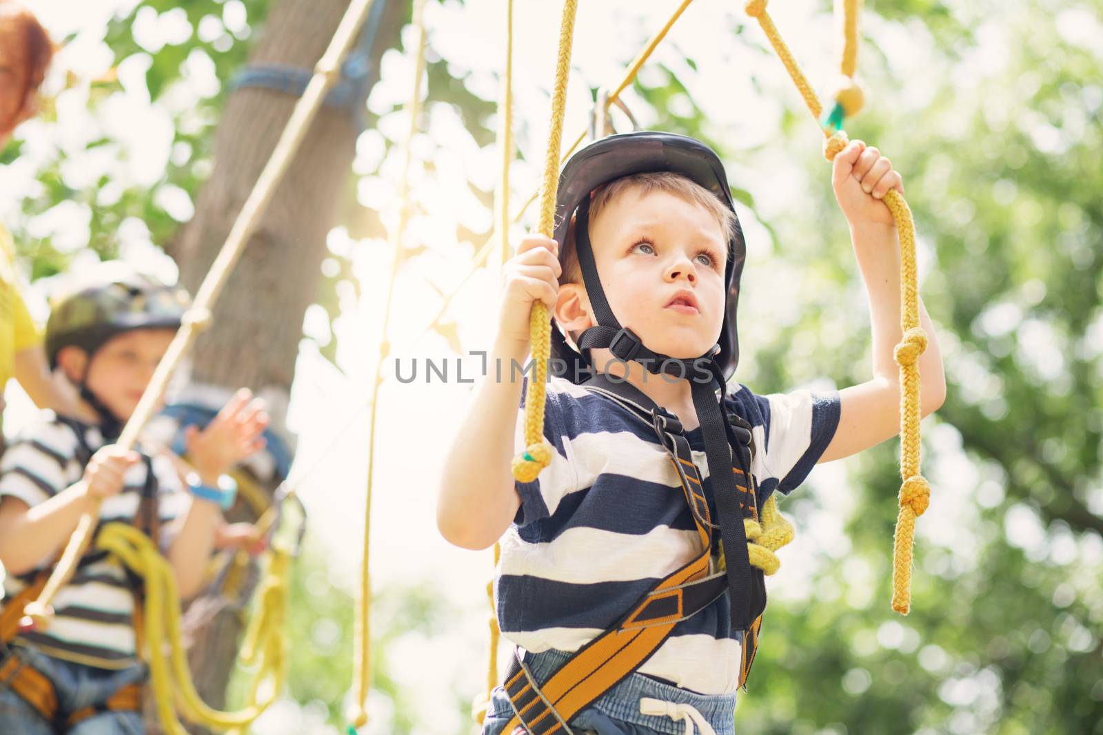 Kids climbing in adventure park. Boy enjoys climbing in the ropes course adventure. Child climbing high wire park. Happy boys playing at adventure park, holding ropes and climbing wooden stairs.