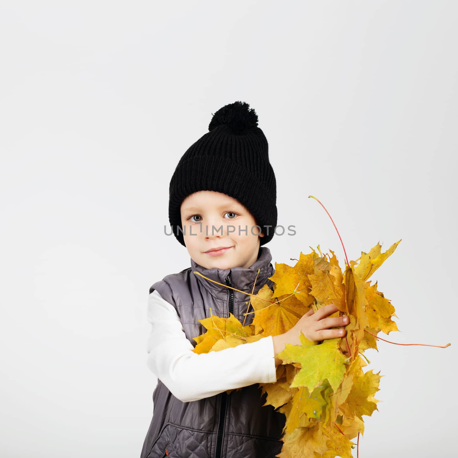 Portrait of happy joyful beautiful little boy against white background. Child holding a yellow maple leaves. Kid throws up a autumn yellowed foliage