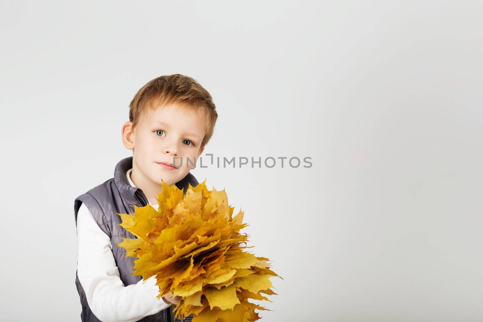 Portrait of happy joyful beautiful little boy against white background. Child holding a yellow maple leaves. Kid throws up a autumn yellowed foliage