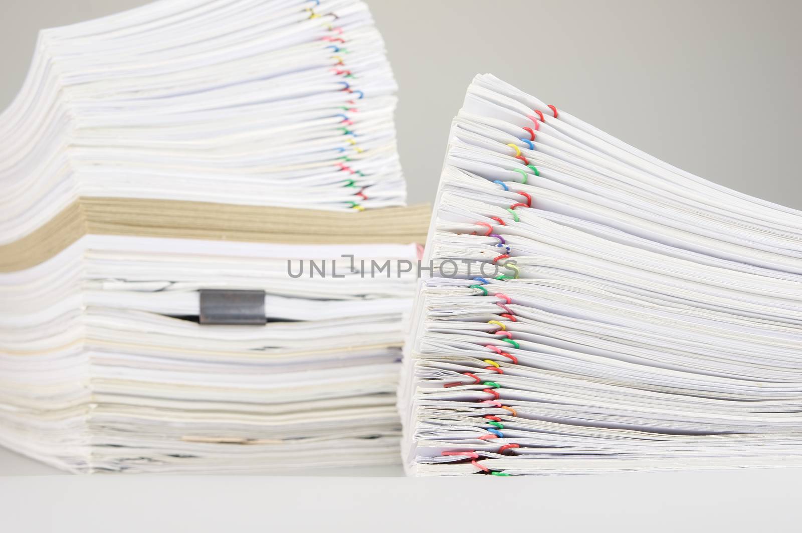 Pile overload paper of receipt and report with colorful paperclip have blur pile document and brown envelope as background on white table.