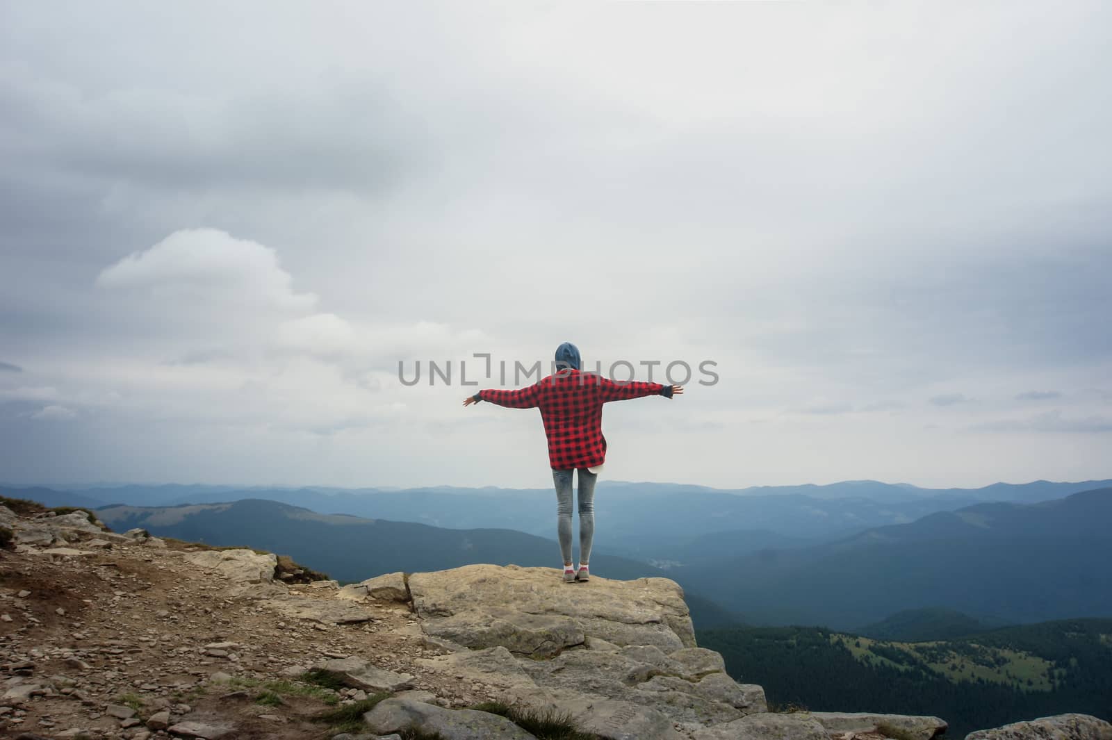 Girl standing on top of the hill balancing and spreading hands in front of beautiful mountain scenery