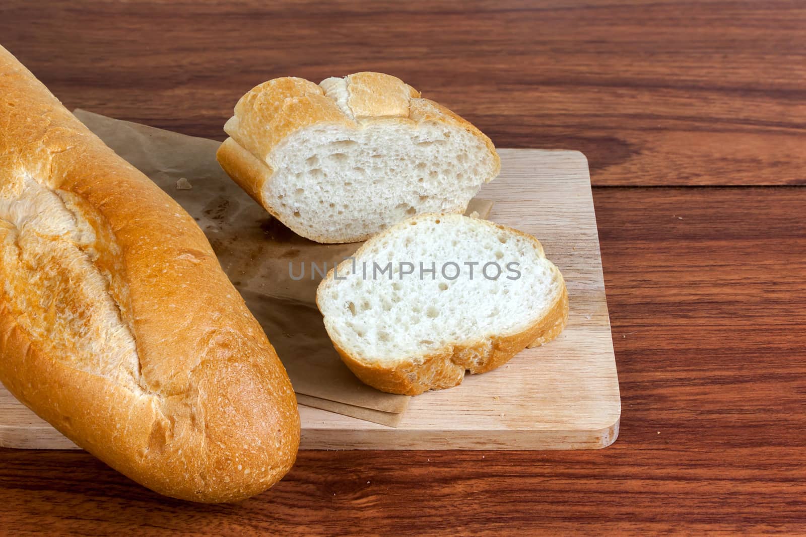 French bread baguette cut on brown paper with wooden board