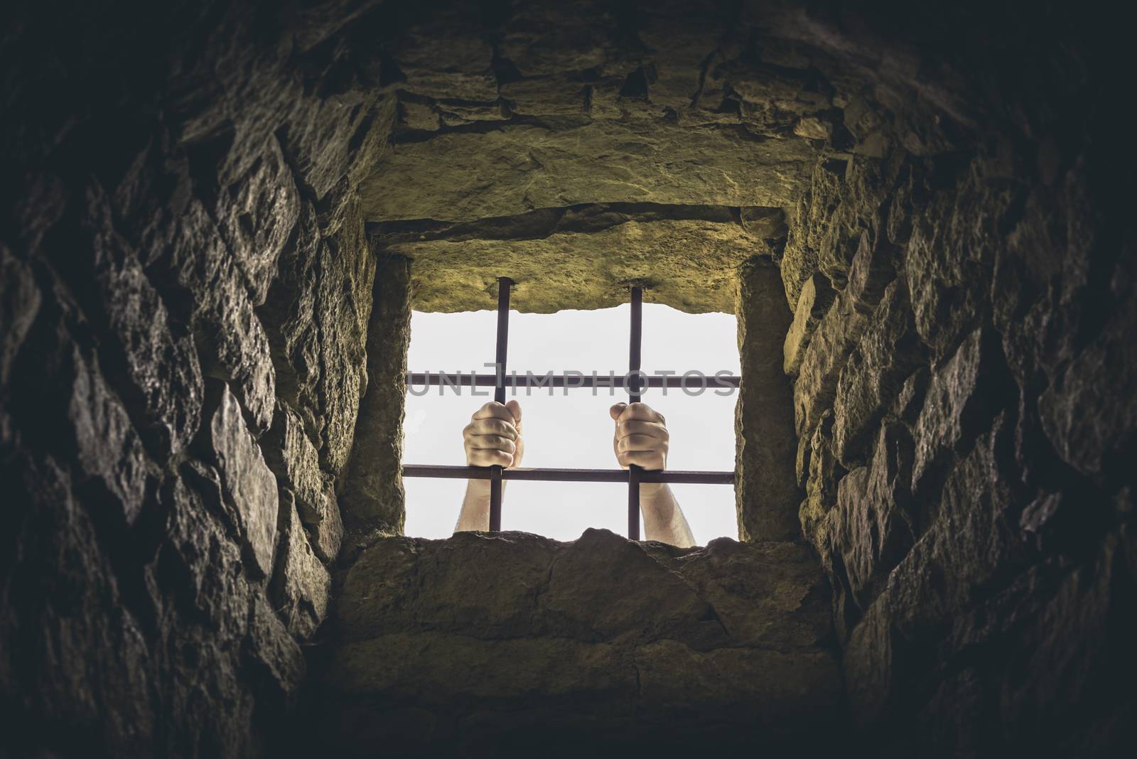 Conceptual image with a man's hand grabbing the metal bars from an old medieval prison