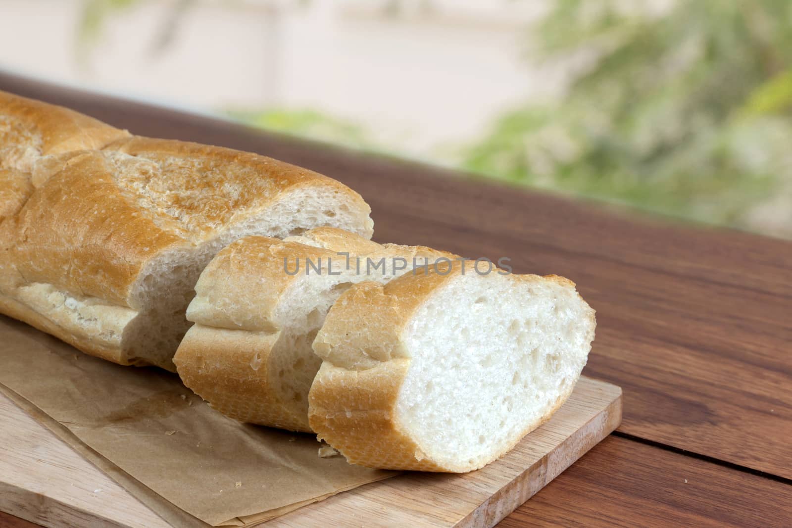 French bread baguette cut on brown paper with wooden board