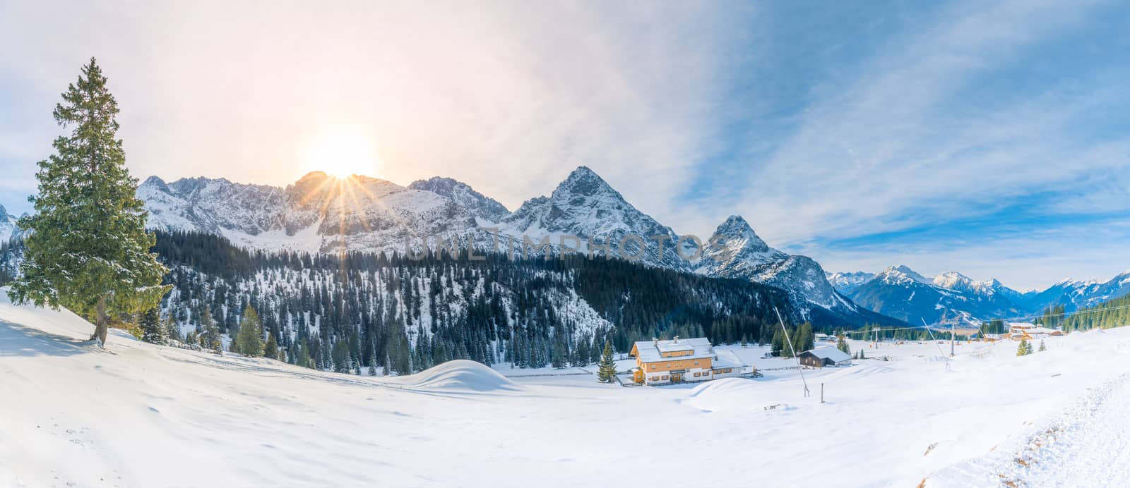 Winter fairytale scenery with a small Austrian village, evergreen fir trees and the Alps covered in snow, on a sunny day of December.