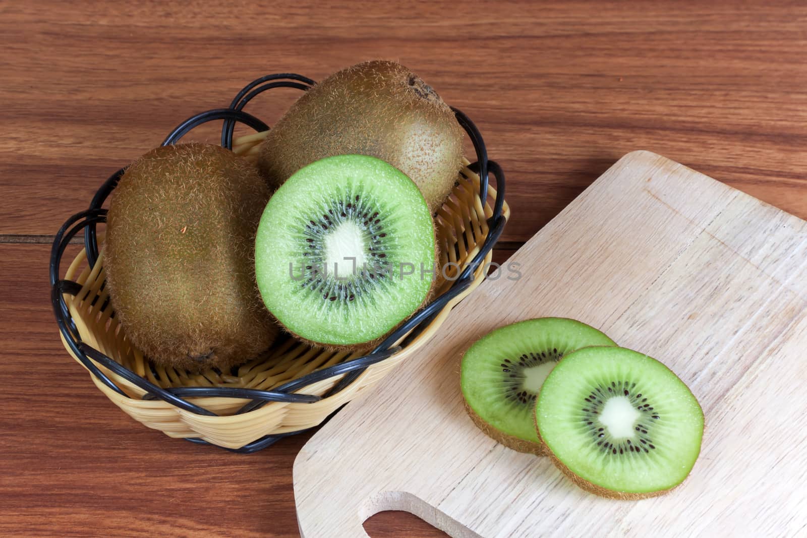 fresh kiwi  fruits and slices of kiwi fruit in basket on wood