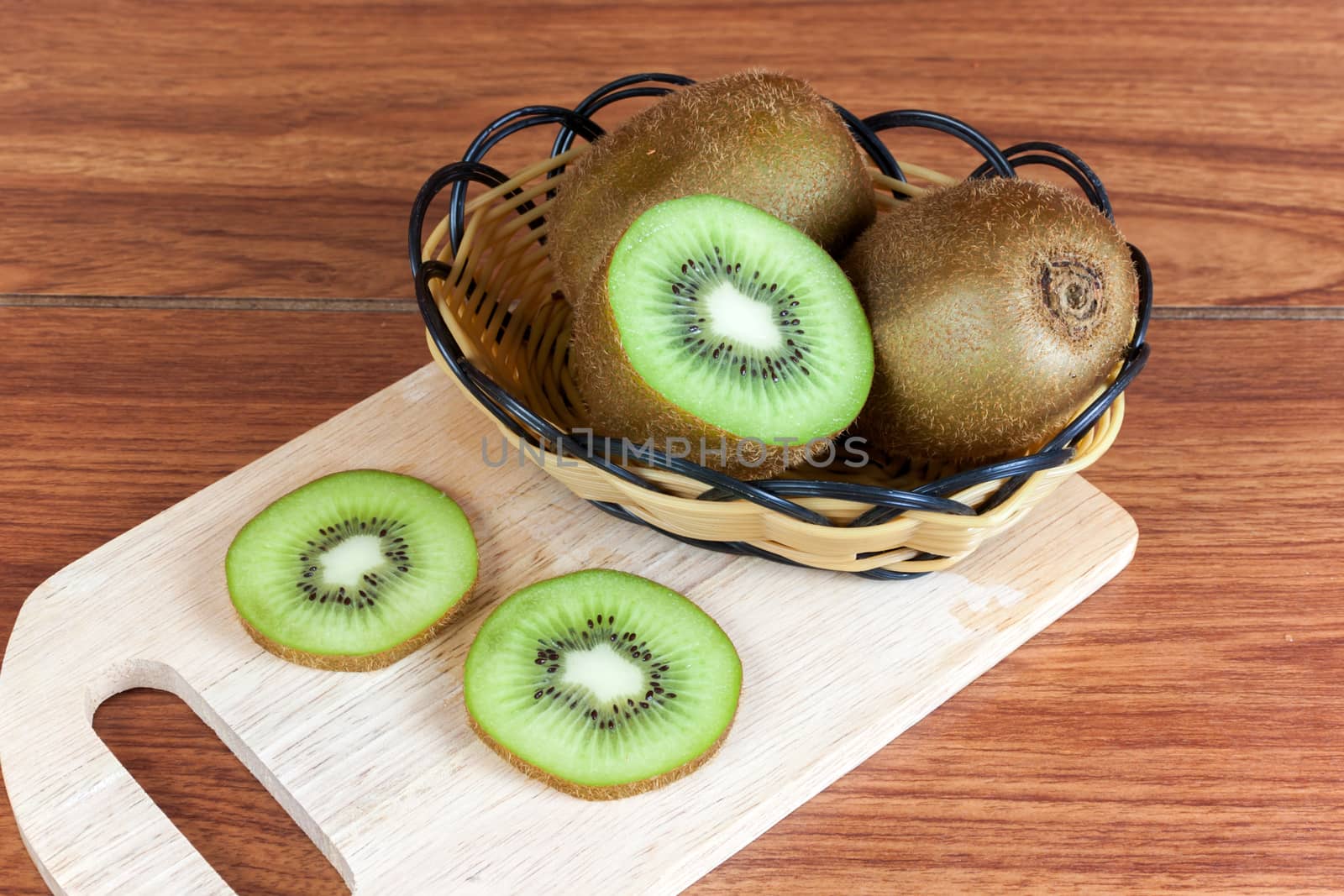 fresh kiwi  fruits and slices of kiwi fruit in basket on woodh