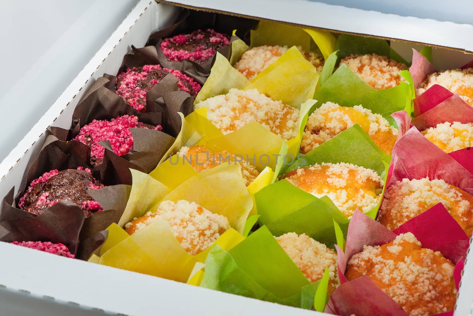The muffins of different color packed into color paper and into a cardboard box
