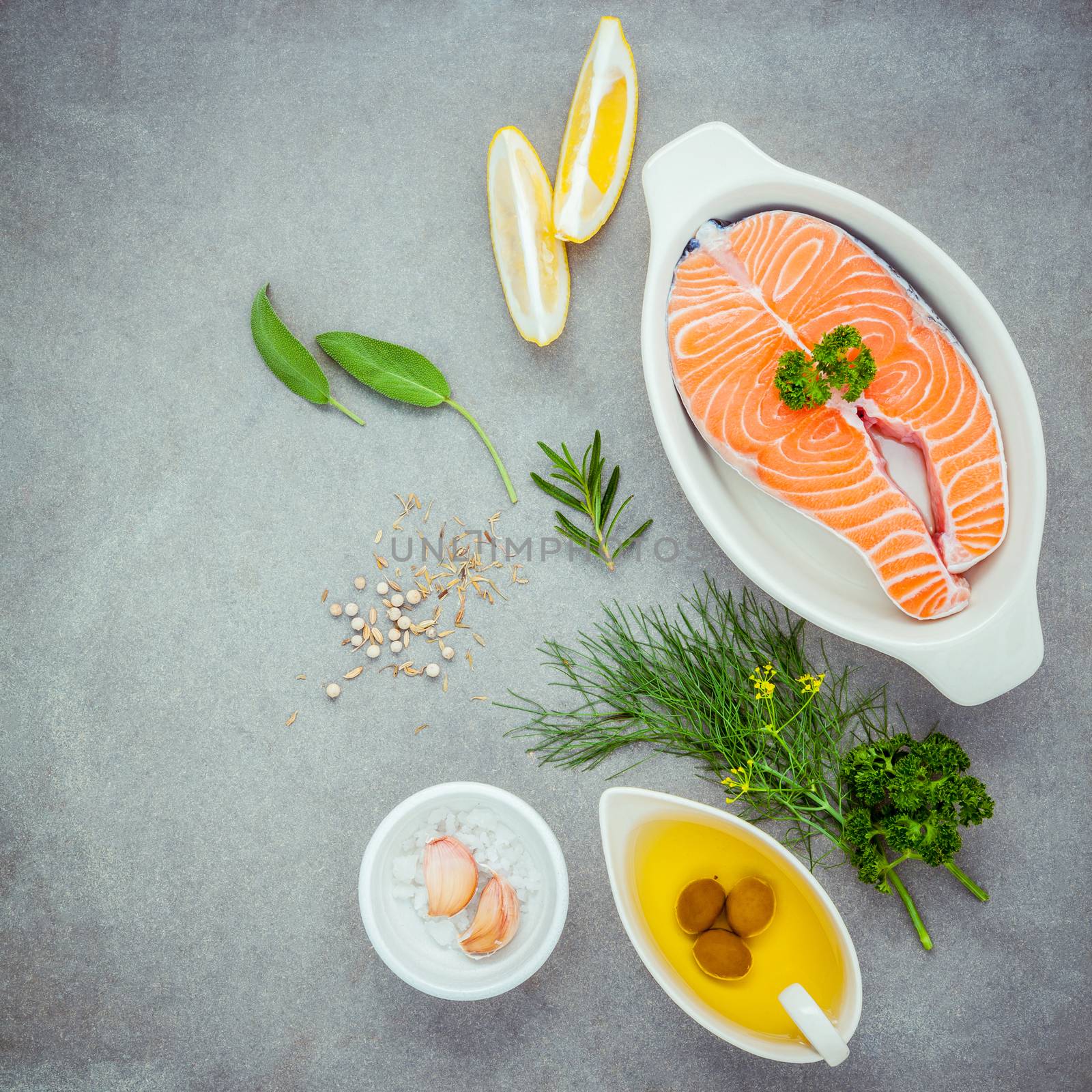 Raw salmon fillet in the white bowl with ingredients olive oil ,sea salt, and herbs  fennel ,sage ,rosemary ,garlic ,pepper and lemon for cooking on concrete background .