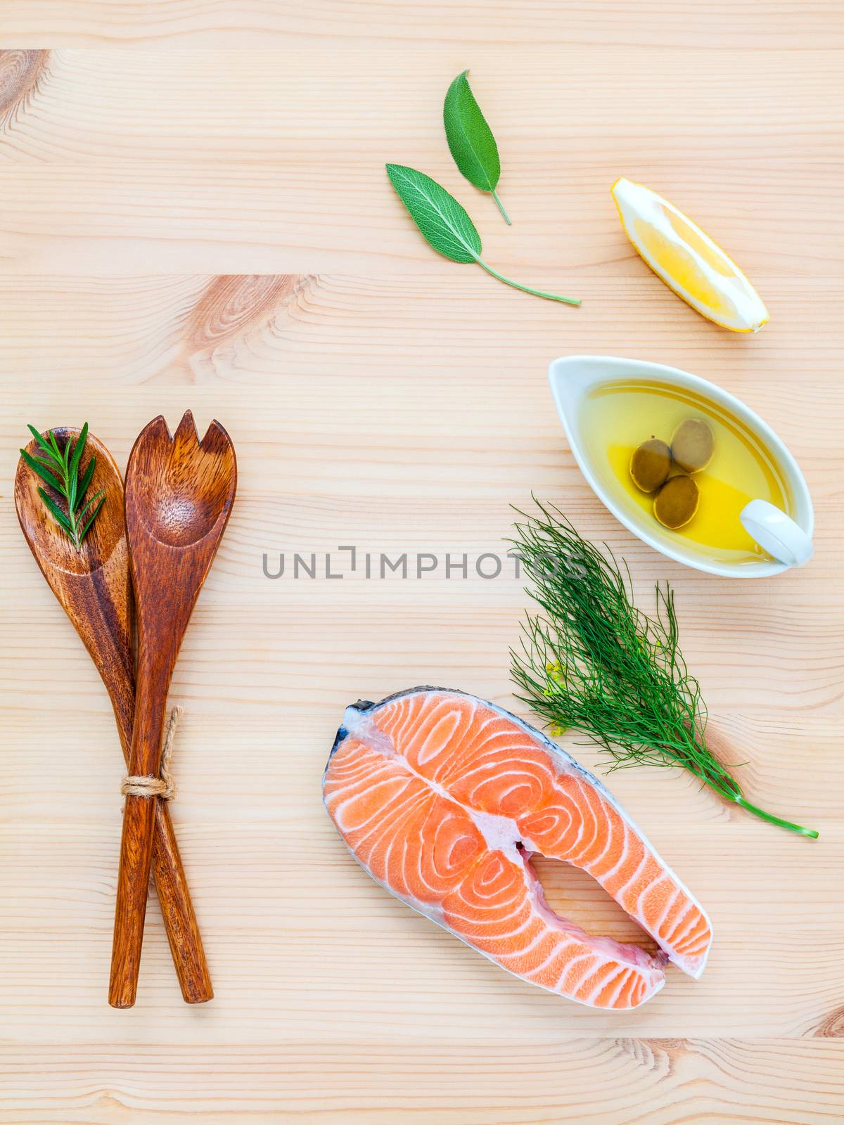 Raw salmon fillet in the white bowl with ingredients olive oil ,sea salt, and herbs  fennel ,sage ,rosemary ,garlic ,pepper and lemon for cooking on wooden background .