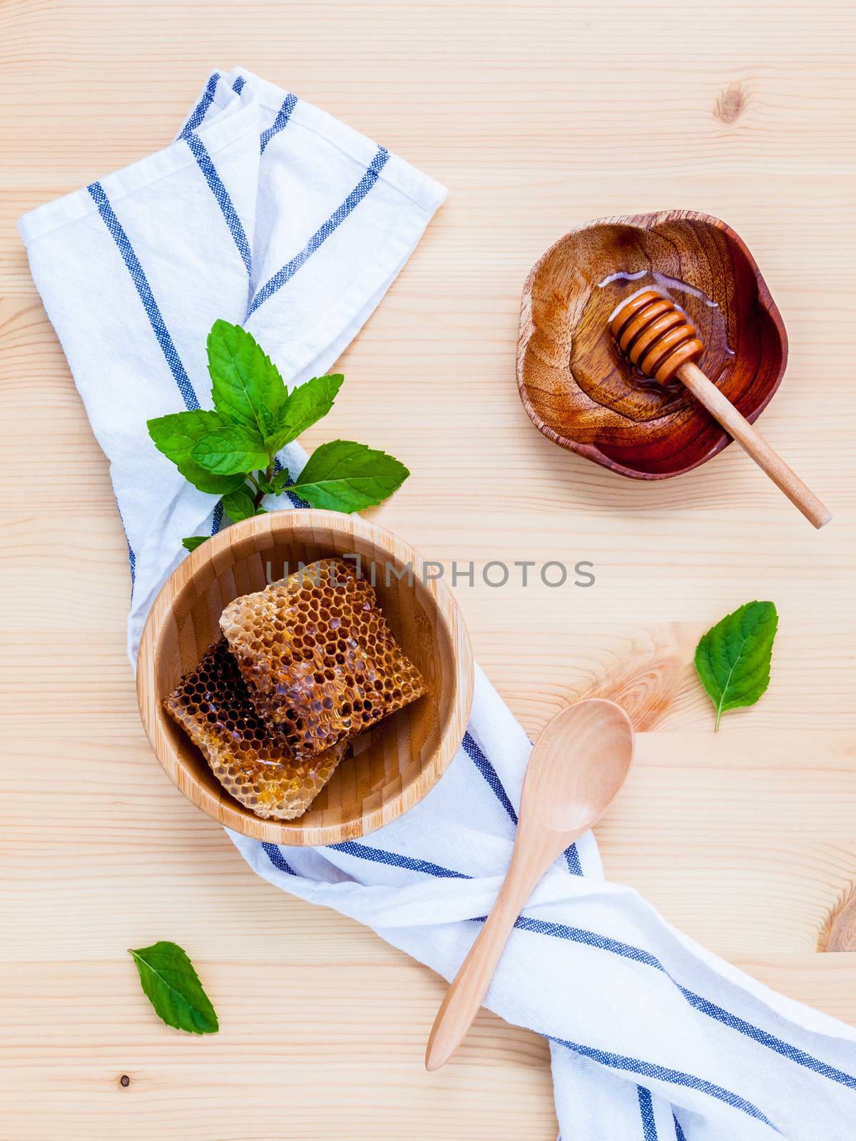 Honeycomb and honey in wooden bowl with peppermint set up on whi by kerdkanno