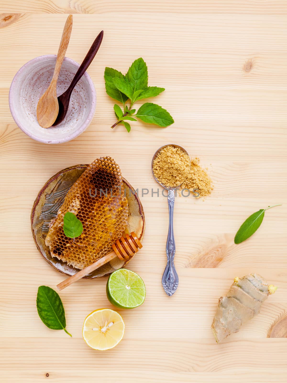 Honeycomb in wooden bowl with herbs mint ,thyme and sage set up on white wooden background.