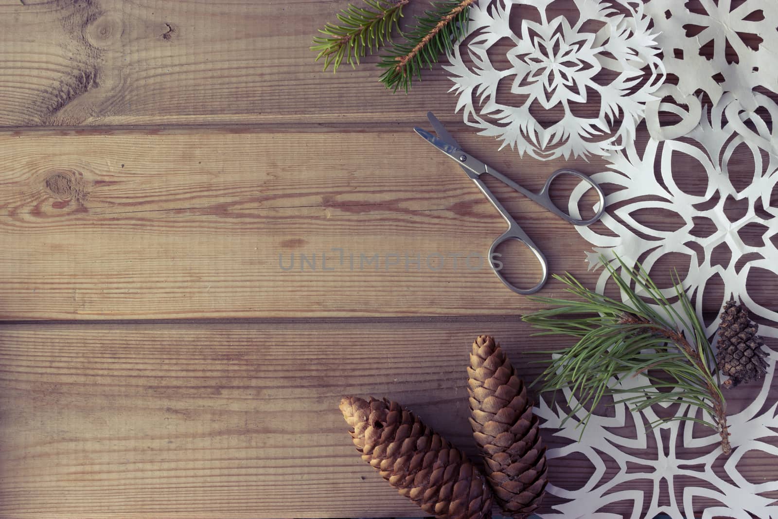 handmade paper snowflakes Christmas tree branches and fir-cones on wooden table