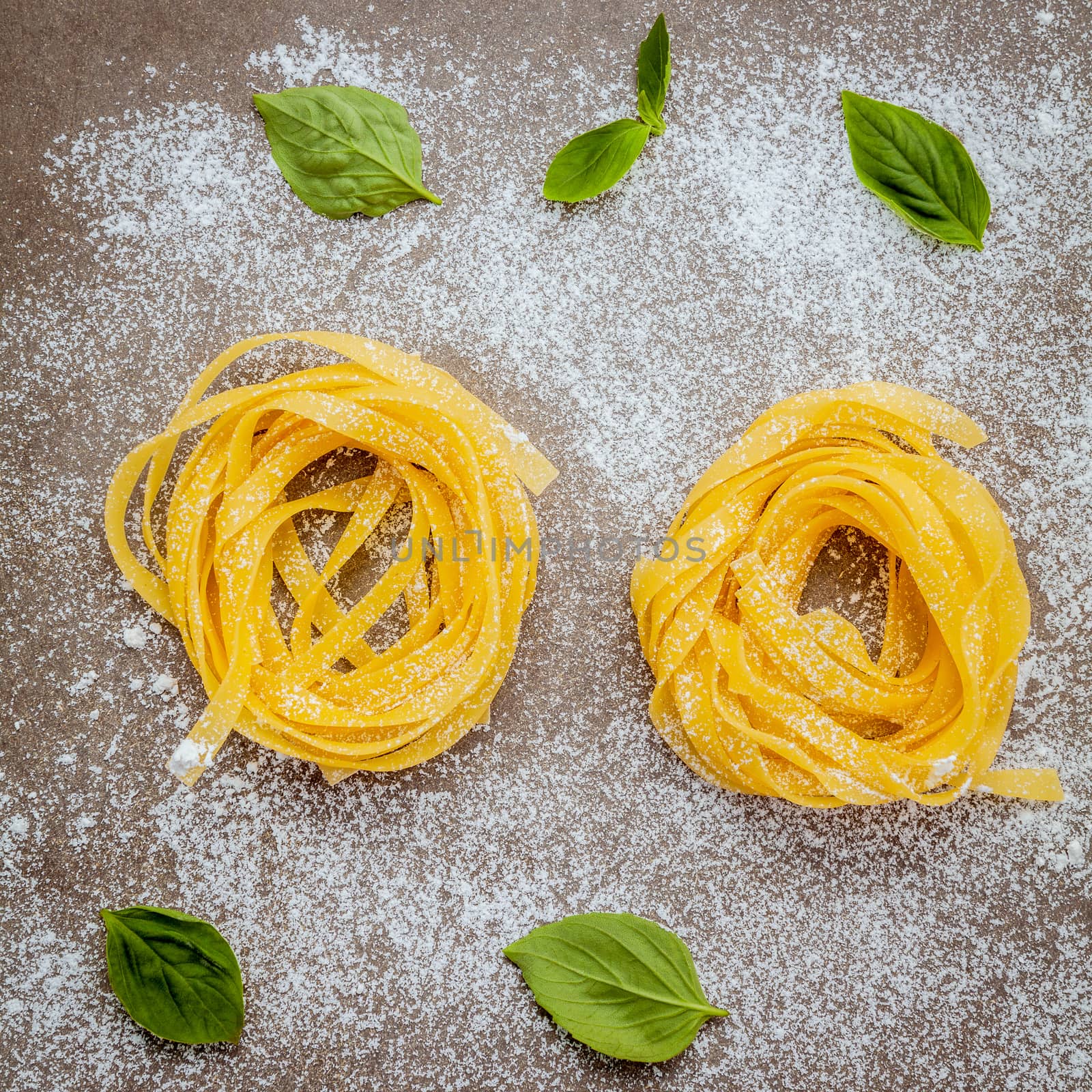 Italian food concept pasta with sweet basil with flour setup on concrete background. Homemade tagliatelle. Raw pasta on the concrete background. Food background top view .