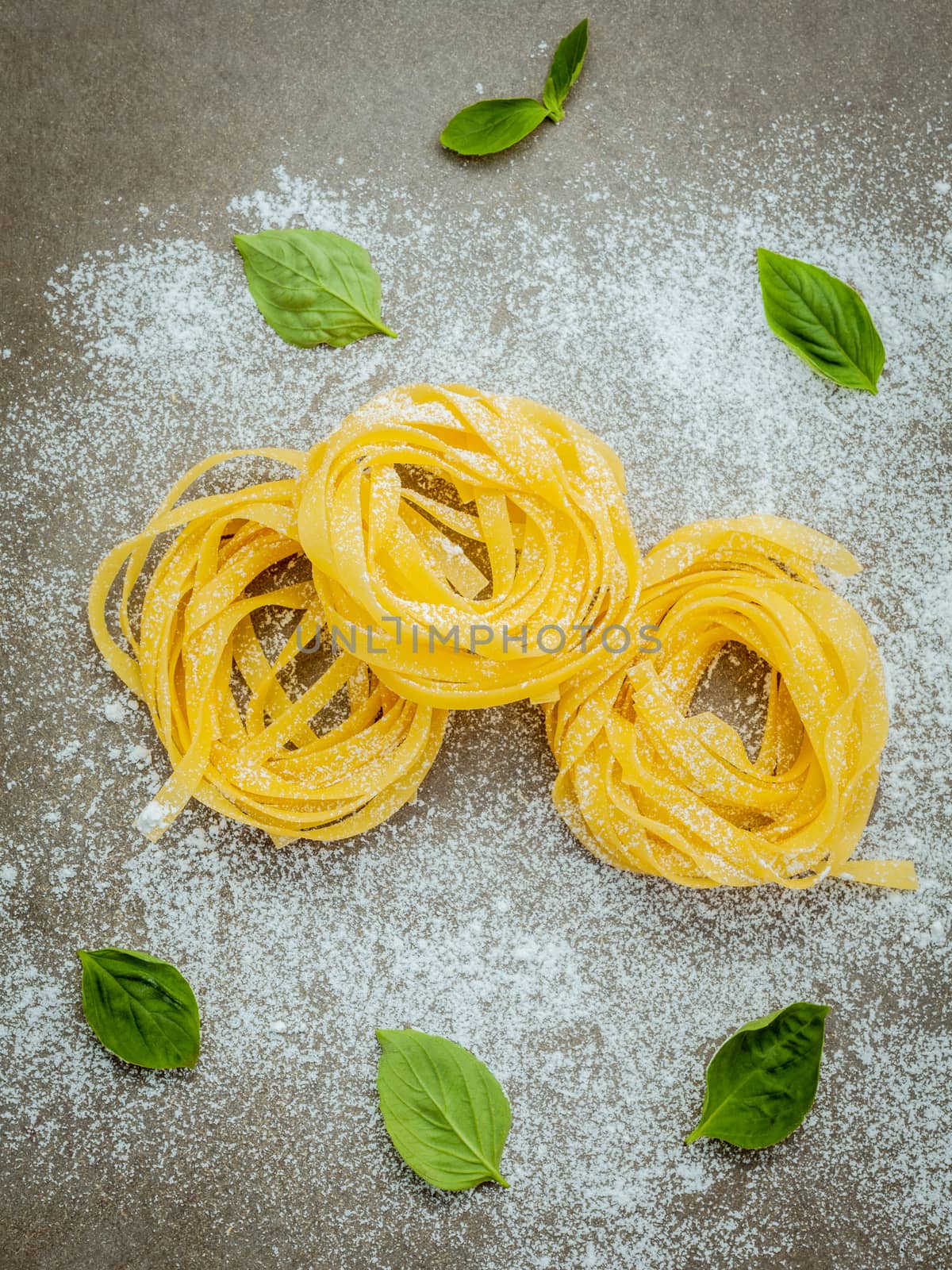 Italian food concept pasta with sweet basil with flour setup on concrete background. Homemade tagliatelle. Raw pasta on the concrete background. Food background top view .