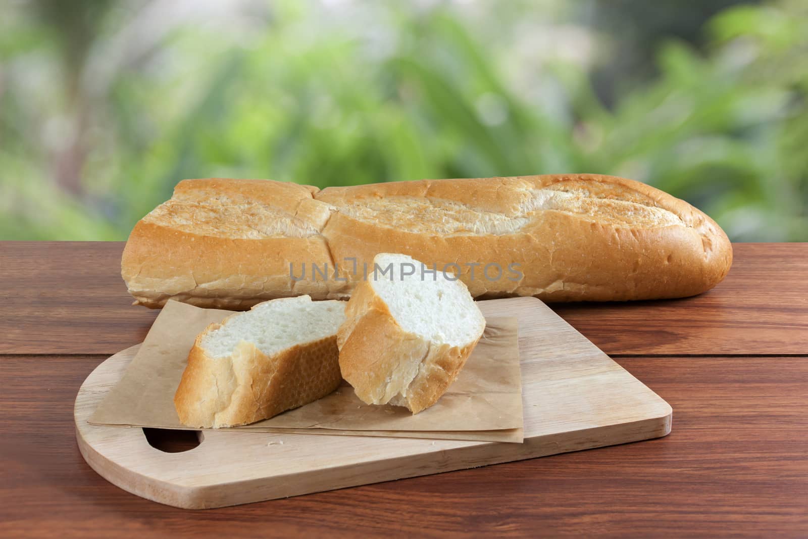 French bread baguette cut on brown paper with wooden board