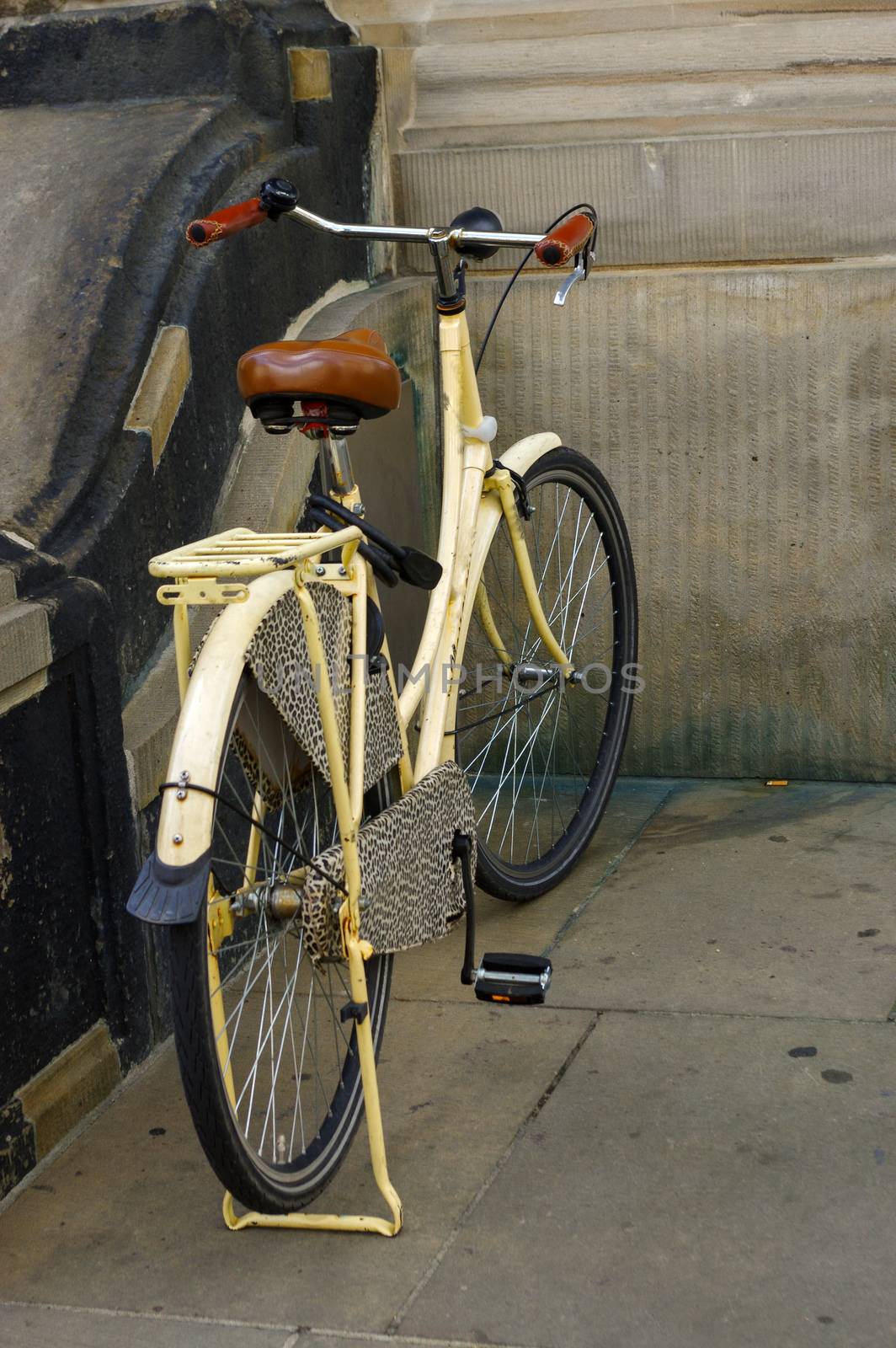 an old yellow bicycle. leather seat with shock absorbers and wheel in front of a church
