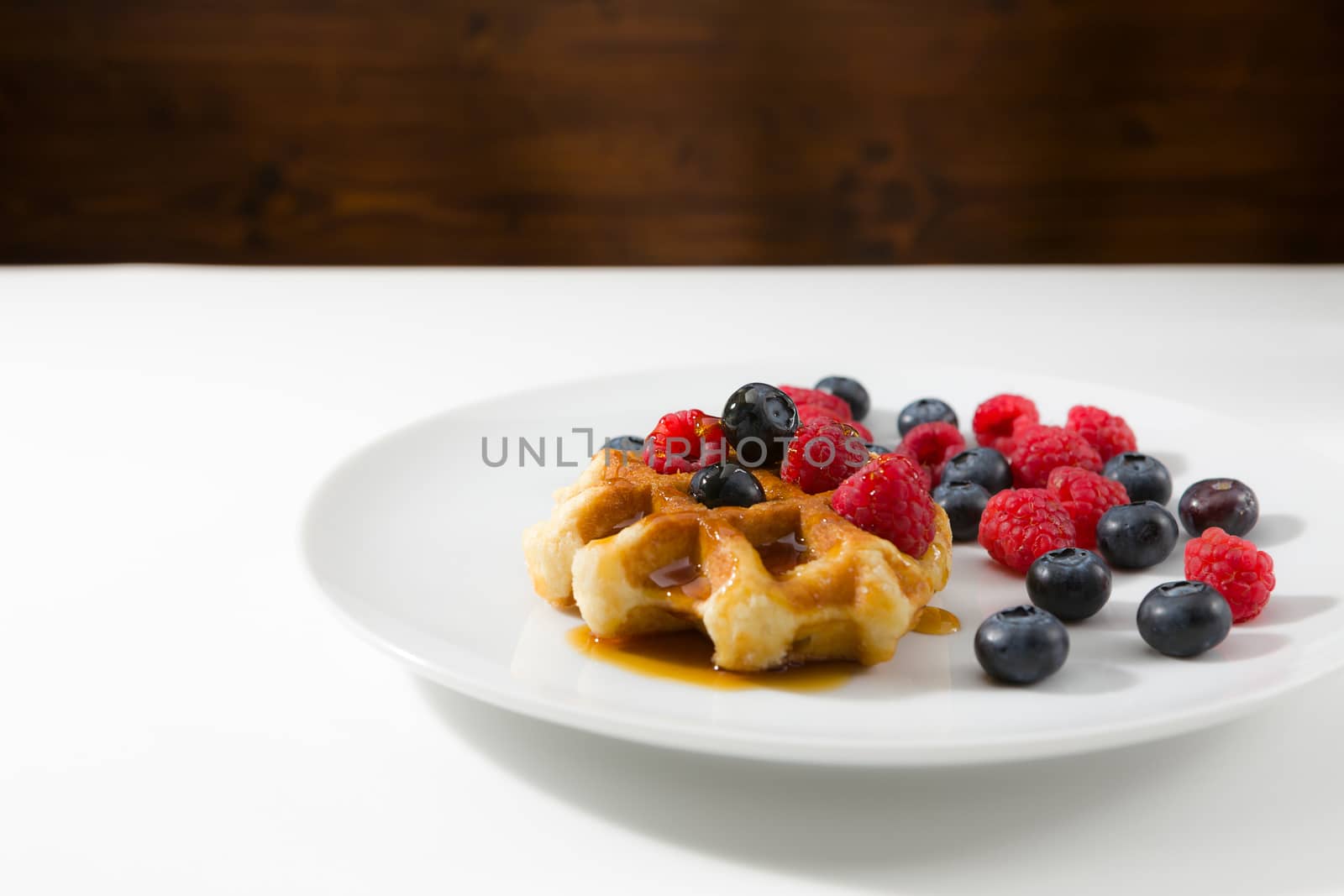 Waffles with fresh ripe berries over a white plate and wooden background