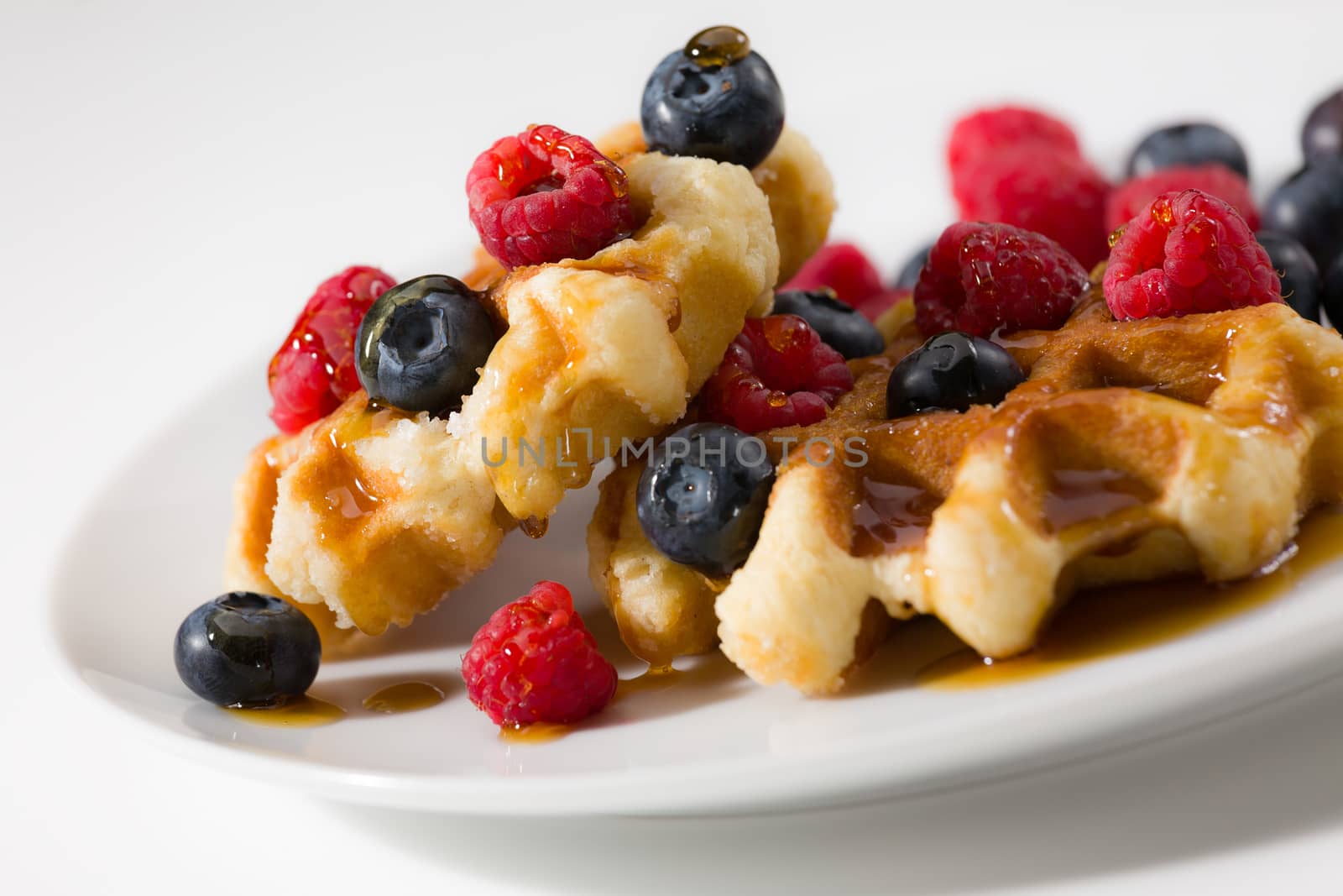 Close-up of waffles with berries and maple syrup over a white plate