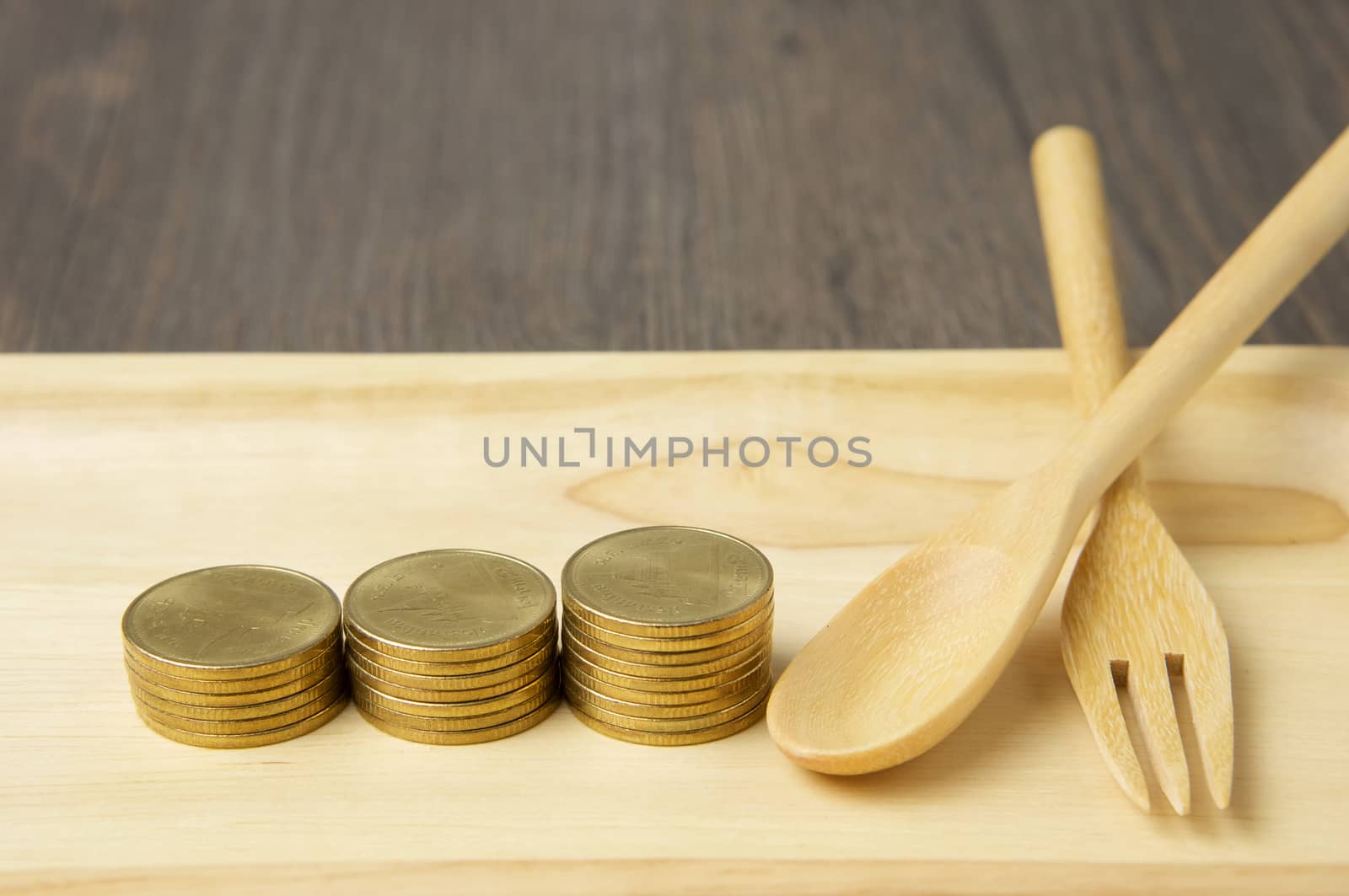 Close up step of gold coins and spoon with fork place on wooden tray with wood background.