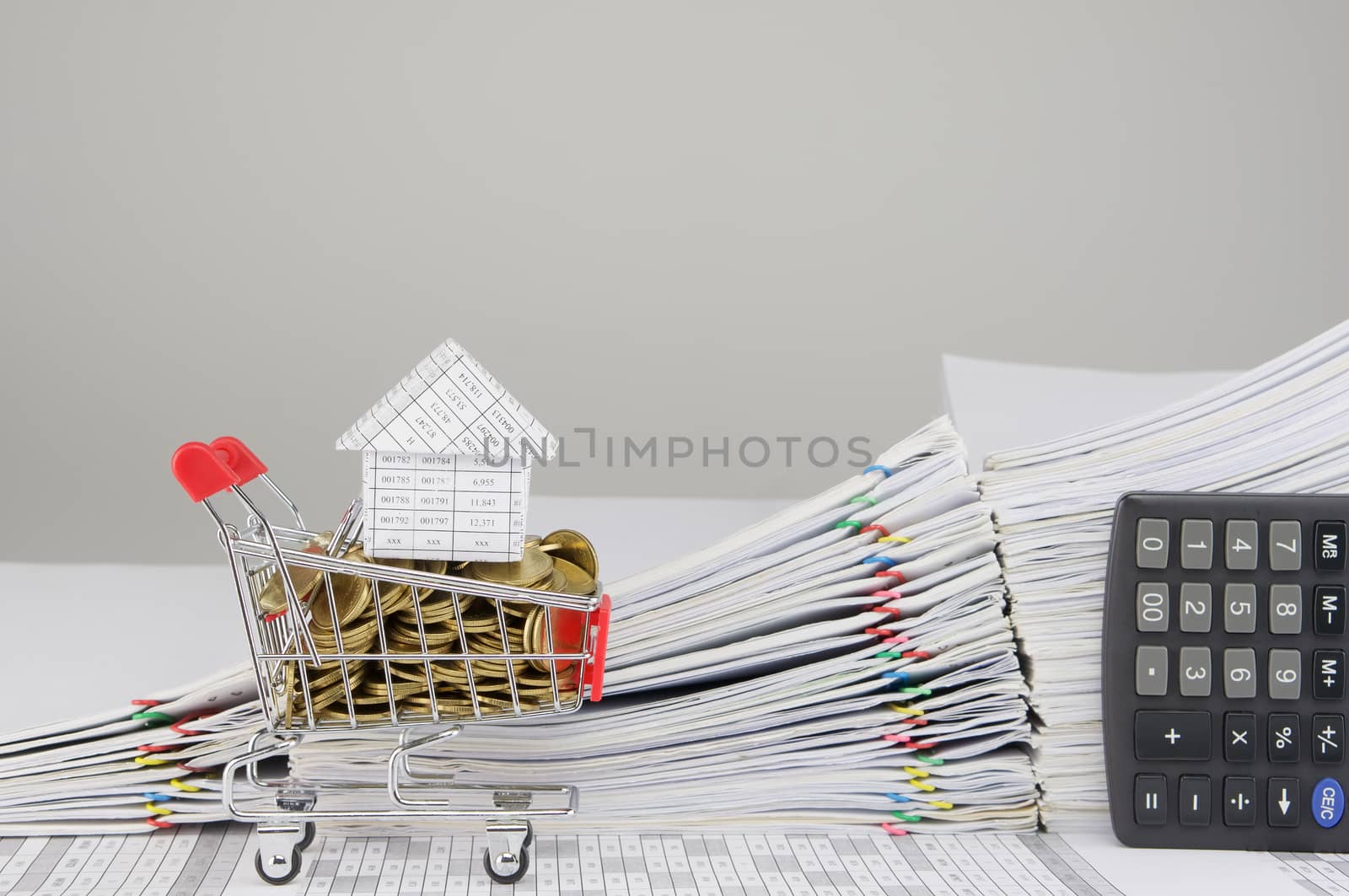 House on shopping cart with gold coins on finance account have blur pile overload document of report and receipt with colorful paperclip with calculator place vertical as background.