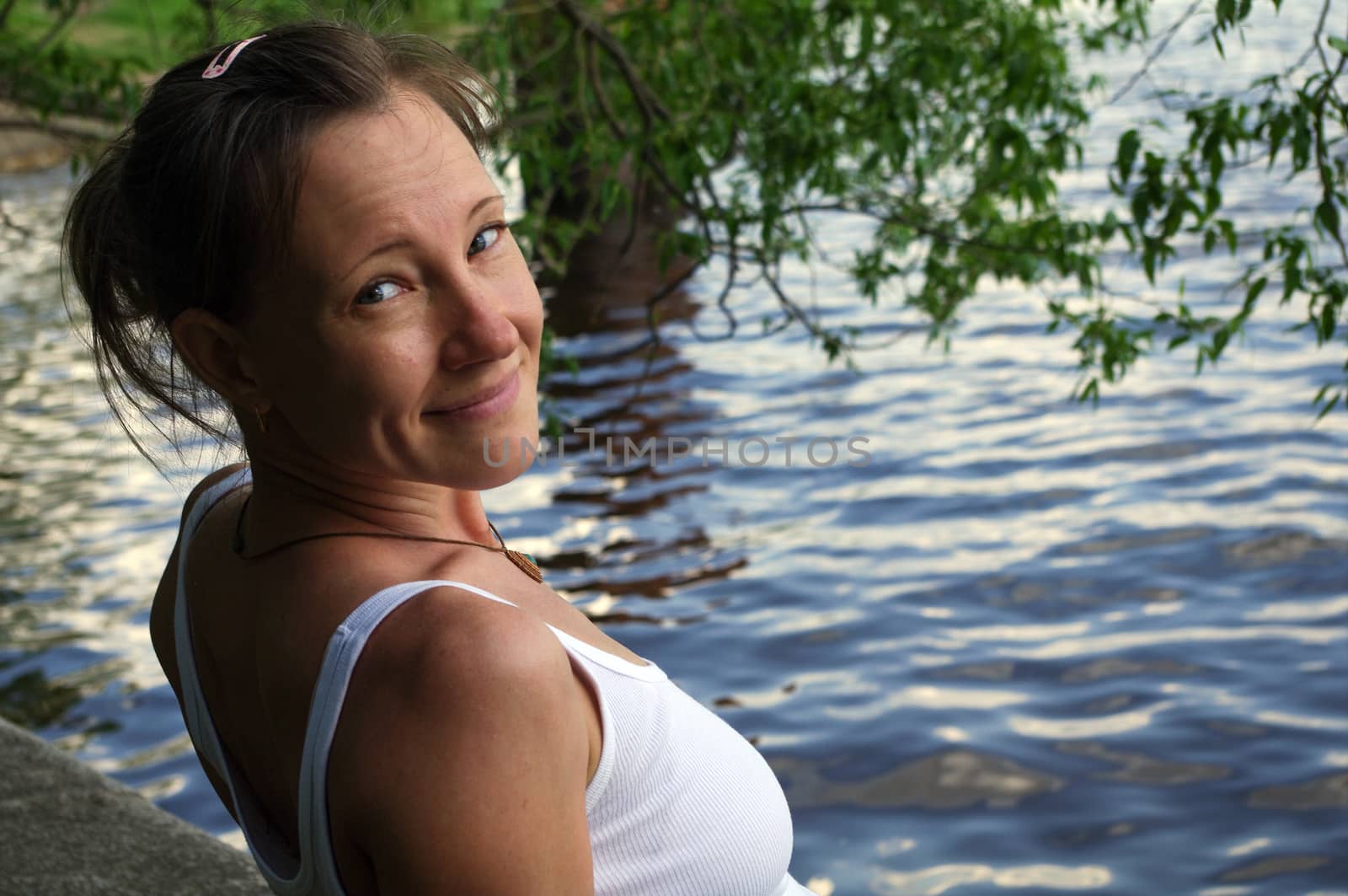 a happy beautiful young woman smiling and looking at camera, standing near water on lake