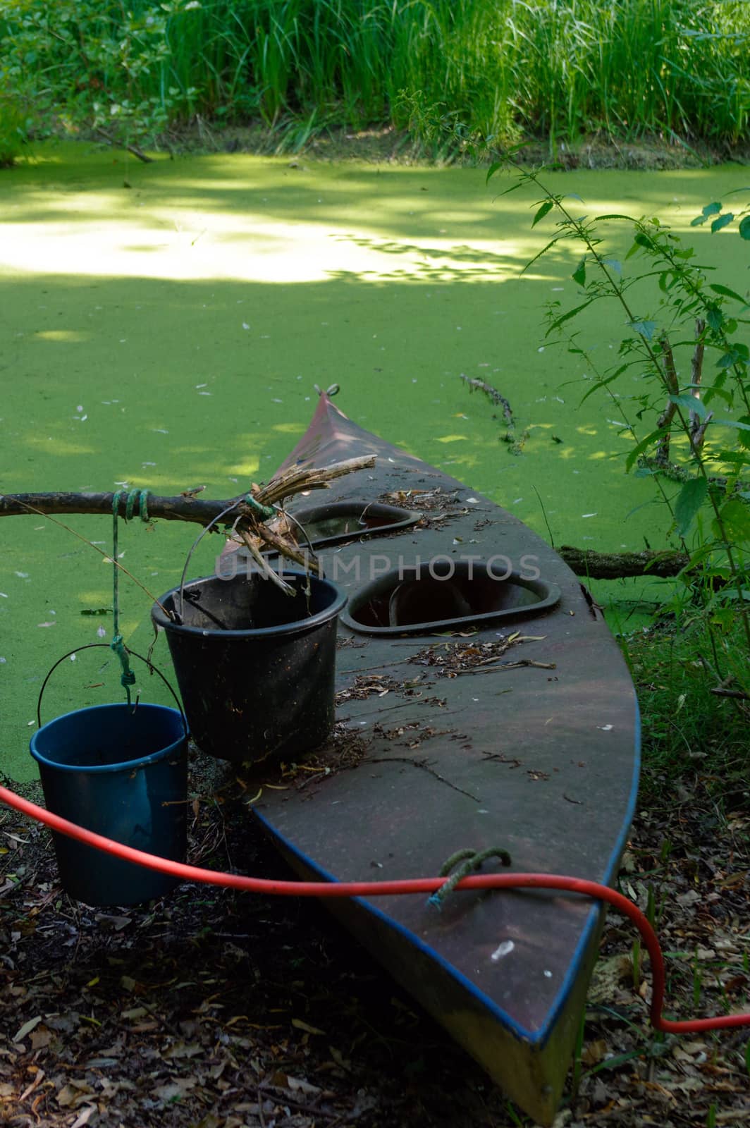 Old canoe ashore the pond with bucket on it by evolutionnow