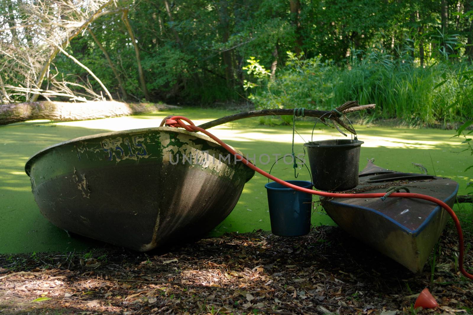 Old canoe and a wooden boat ashore the pond with bucket on it by evolutionnow