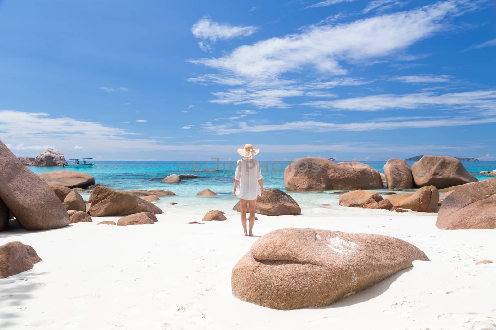 Woman wearing white loose tunic over bikini and beach hat on Anse Lazio beach on Praslin Island, Seychelles. Summer vacations on picture perfect tropical beach concept.